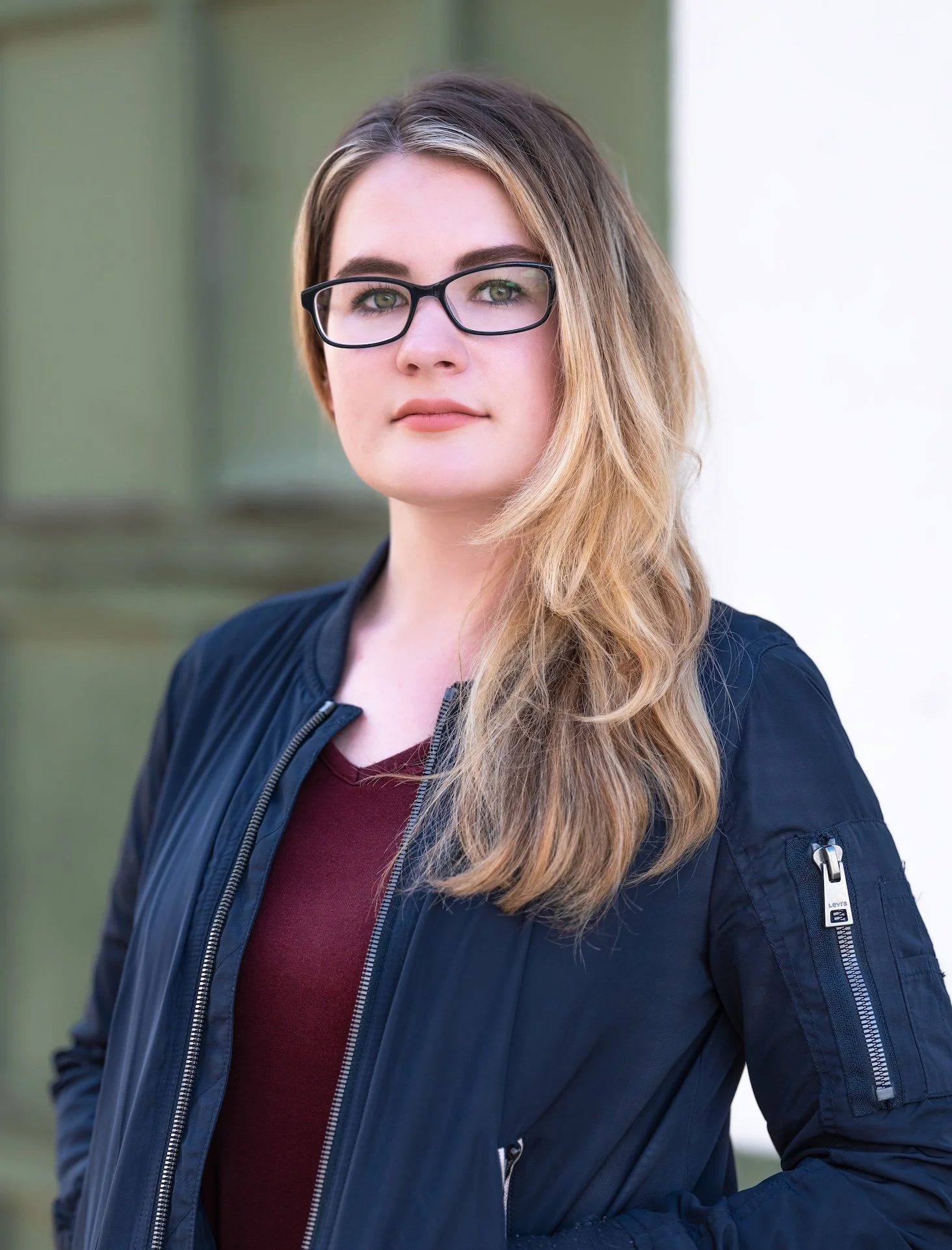 Professional Portrait Photography by Minneapolis Photographer Jay Cupcake. A young woman with glasses and long, wavy hair standing outdoors in front of a slightly blurred background.