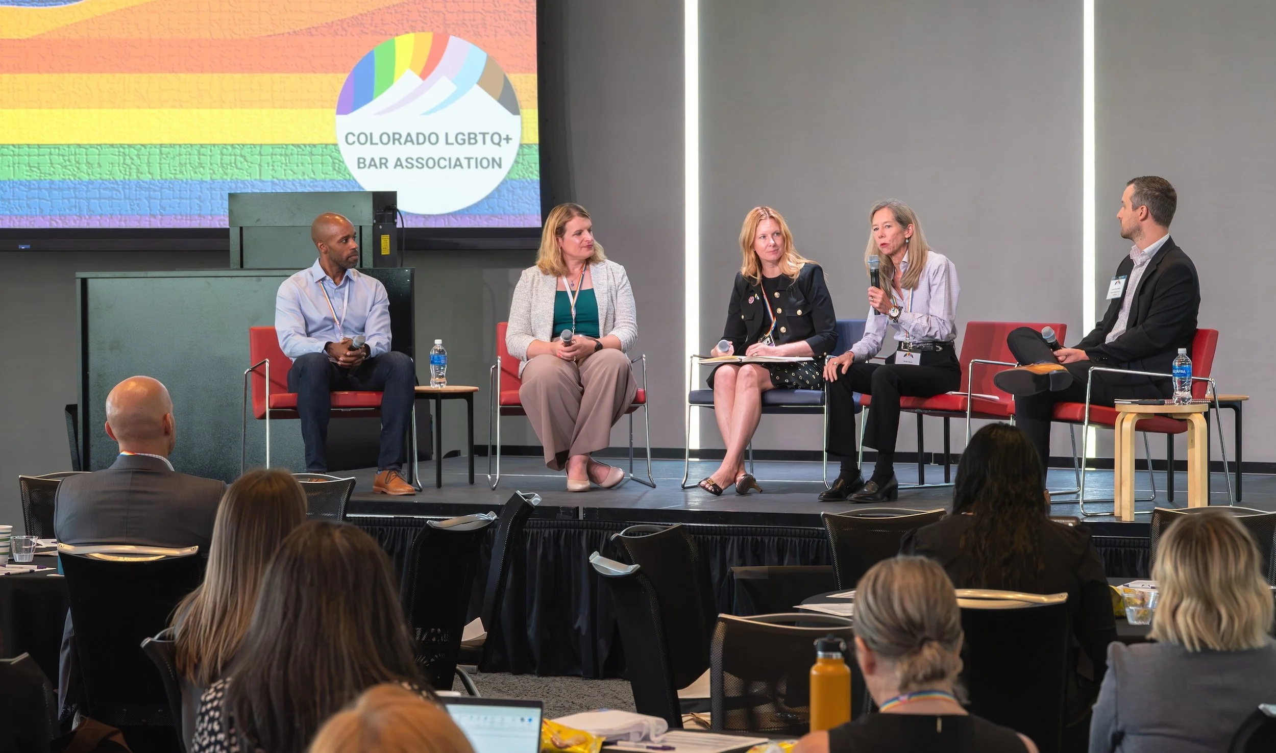 Professional Event Photography by Saint Paul Photographer Jay Cupcake. Panel discussion at a conference with five people sitting on stage, including four women and one man, with the Colorado LGBTQ+ Bar Association logo on a large screen behind them. 