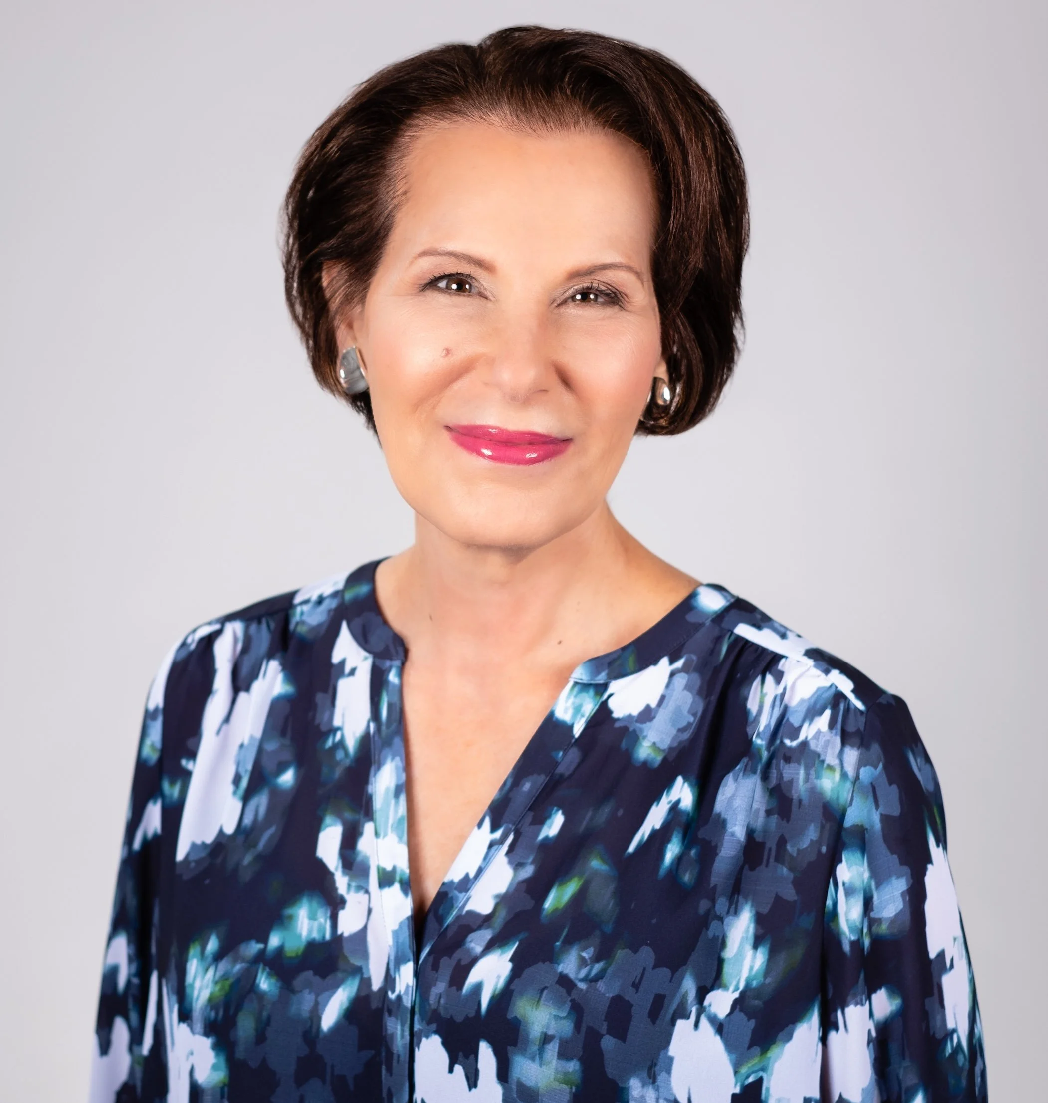 Professional Corporate Headshot by Saint Paul Photographer Jay Cupcake. A professional woman with short brown hair, wearing a blue and white patterned blouse, smiling at the camera against a plain gray background.