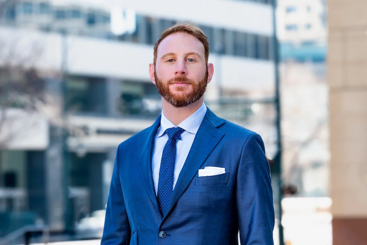 Professional Corporate Headshot by Minneapolis Photographer Jay Cupcake. Businessman in a blue suit and tie standing outside in an urban setting with glass buildings in the background.