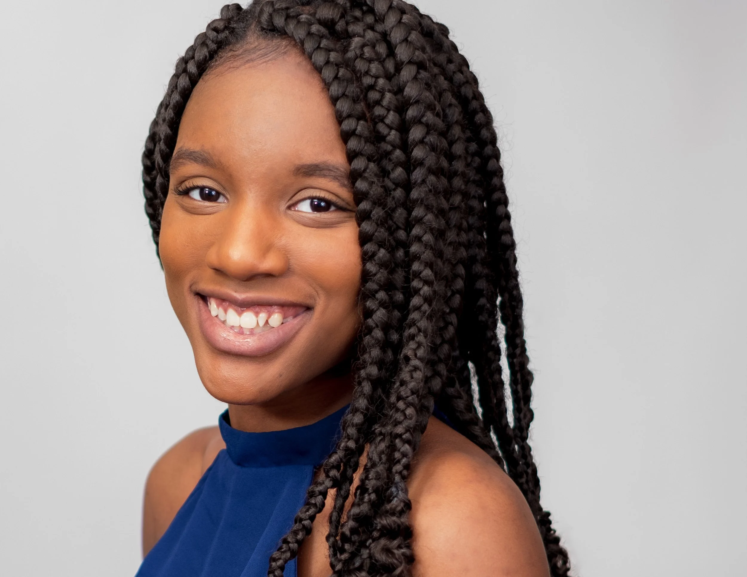 Professional headshot by St. Paul photographer Jay Cupcake. Portrait of a young woman with long braided hair, smiling and wearing a dark blue sleeveless top.