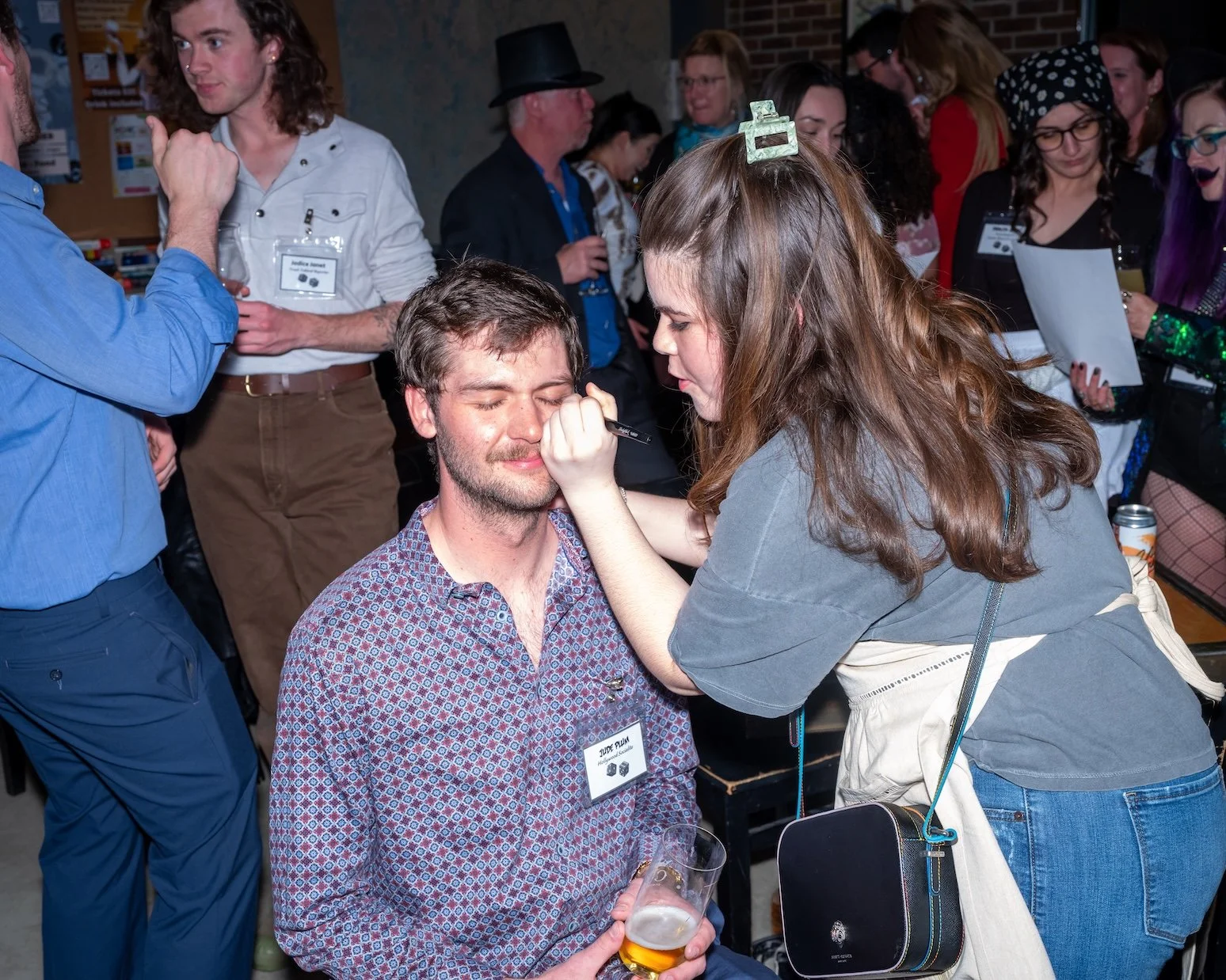 Professional Event Photography by Minneapolis Photographer Jay Cupcake. A woman applying makeup to a man at a social event, with several other people in the background.