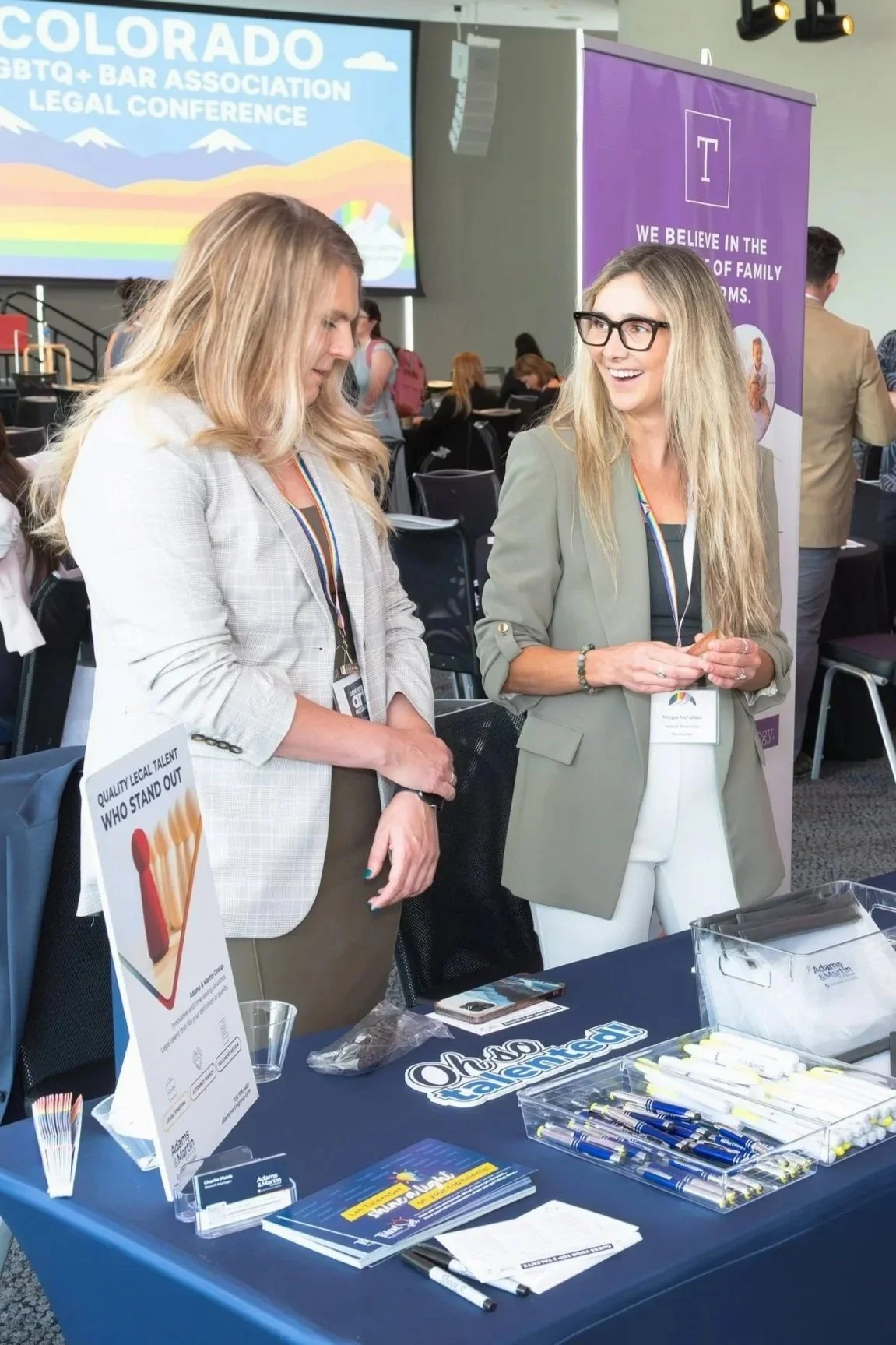 Professional event photography by St. Paul photographer Jay Cupcake. Two women talking at a Colorado LGBTQ+ Bar Association Legal Conference booth with promotional materials on the table.