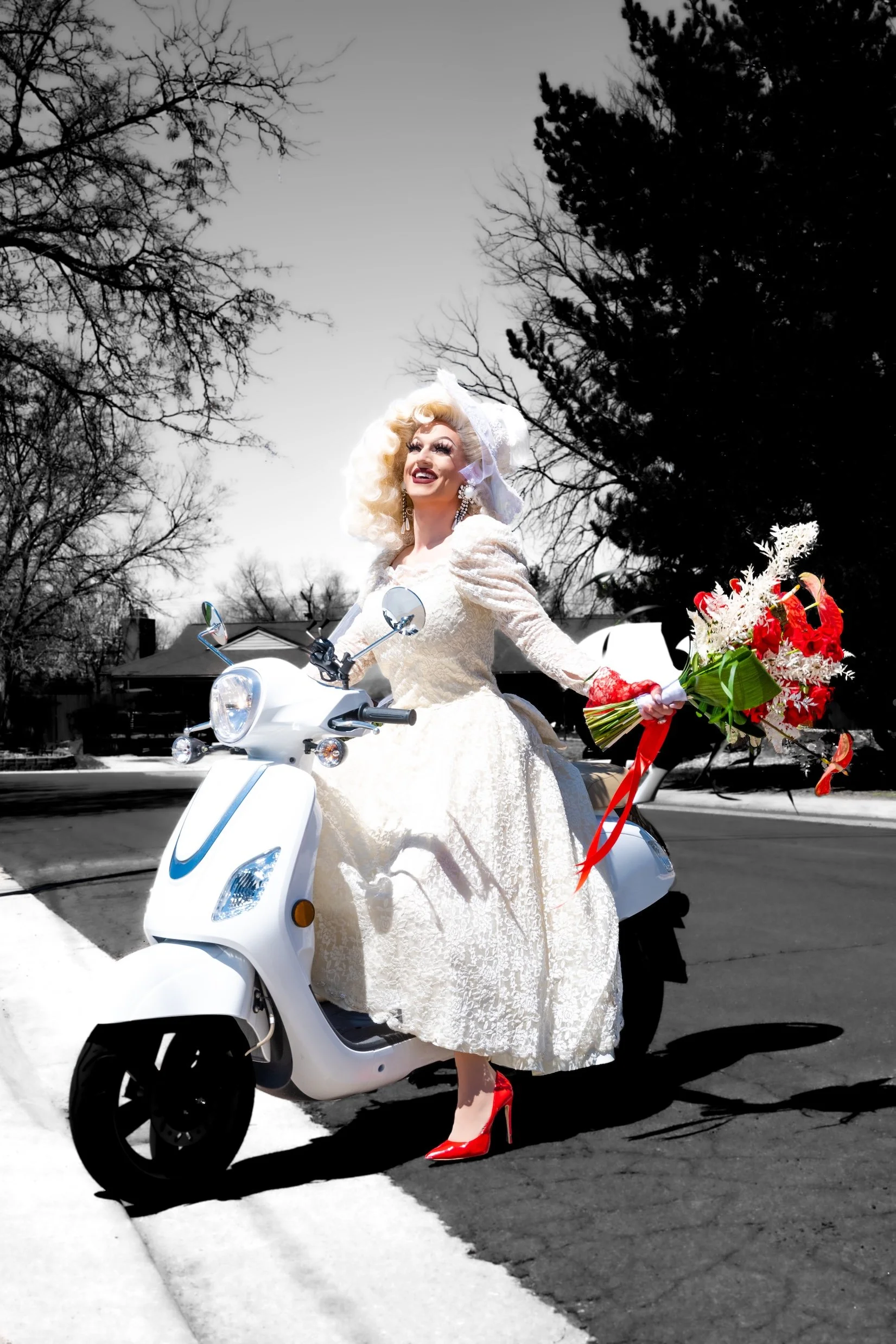 Professional Portrait Photography by Minneapolis Photographer Jay Cupcake. A person dressed as a bride riding a white scooter, holding a bouquet of red and white flowers, with a bright smile, wearing a wedding dress and red high heels, on a street wi