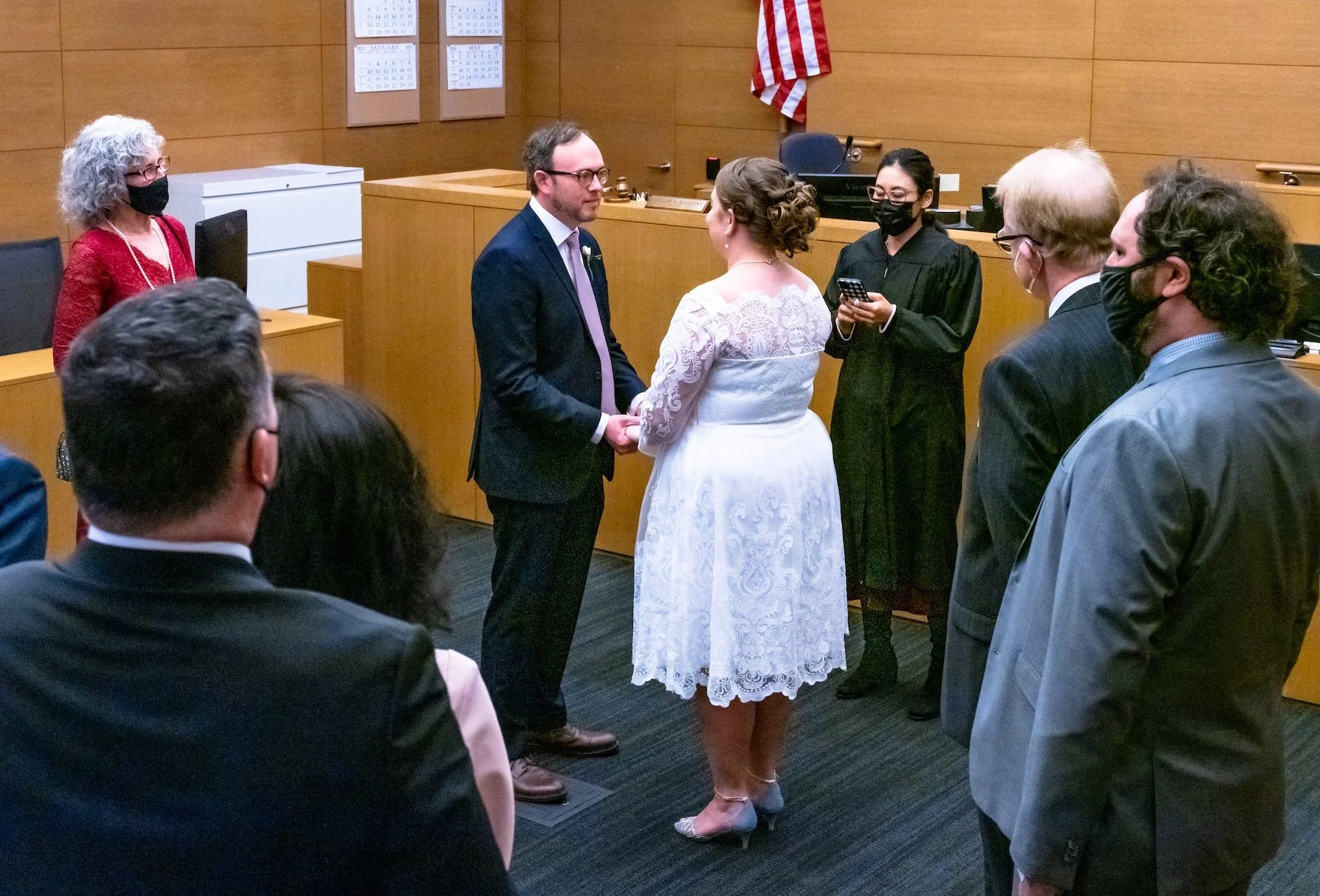 Professional Event Photography by Minneapolis Photographer Jay Cupcake. A wedding ceremony inside a courtroom, with a couple holding hands and facing each other, surrounded by officiant and witnesses all wearing face masks.