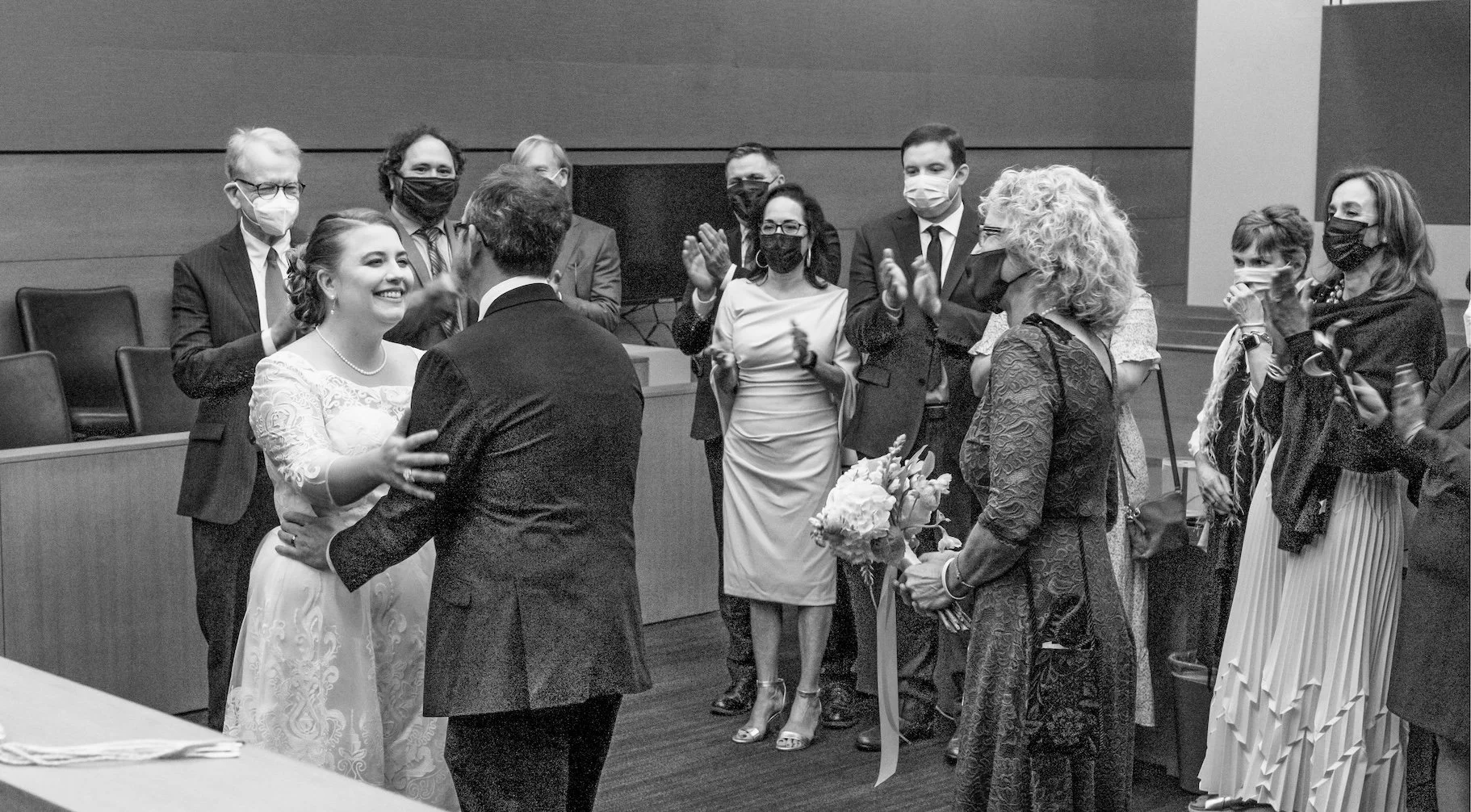 Professional Event Photography by Twin Cities Photographer Jay Cupcake. Black and white photo of a wedding ceremony with a bride and groom exchanging vows, surrounded by wedding guests clapping and smiling. The bride is in a white lace gown holding a