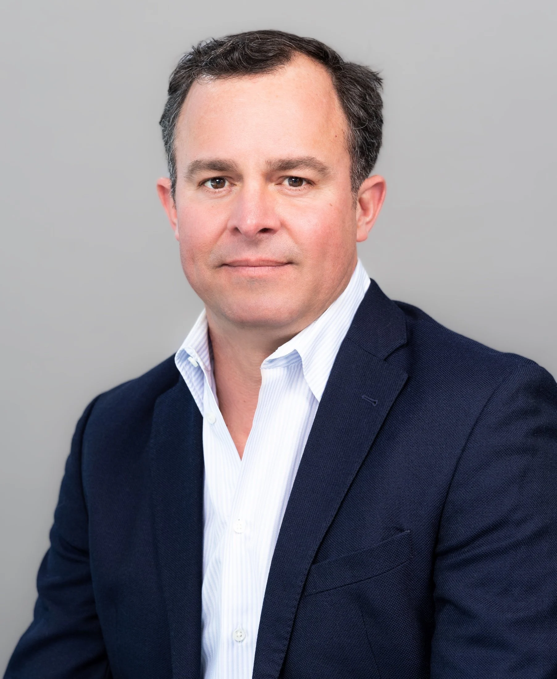 Professional Corporate Headshot by Twin Cities Photographer Jay Cupcake. A professional headshot of a man in a navy suit and white shirt against a gray background