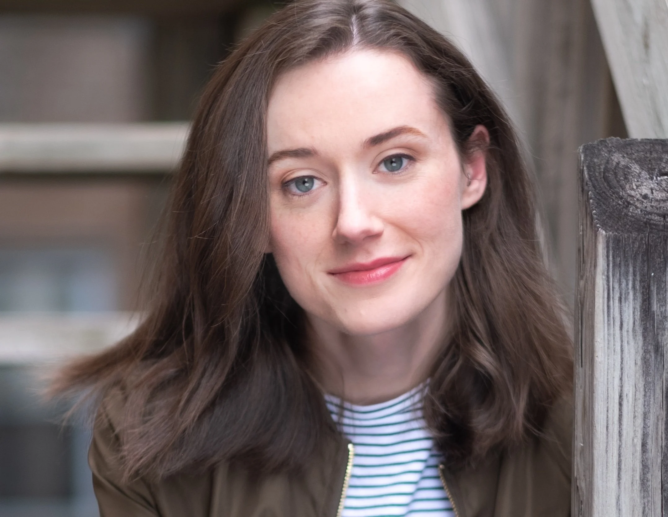 Professional Portrait Photography by Minneapolis Photographer Jay Cupcake. Close-up of young woman with long brown hair and blue eyes smiling outdoors near a wooden structure