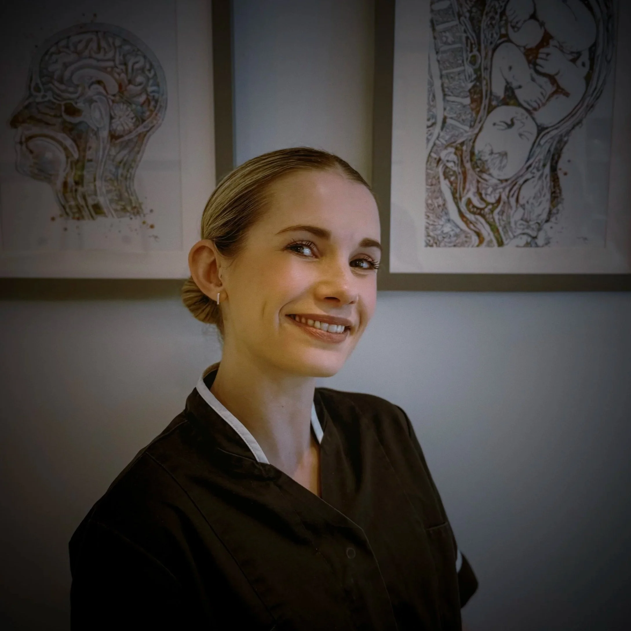 The upper portion of a young woman's face, showing her forehead, eyebrows, and part of her eyes, with her hair pulled back, against a backdrop of two decorative animal-themed illustrations on the wall.