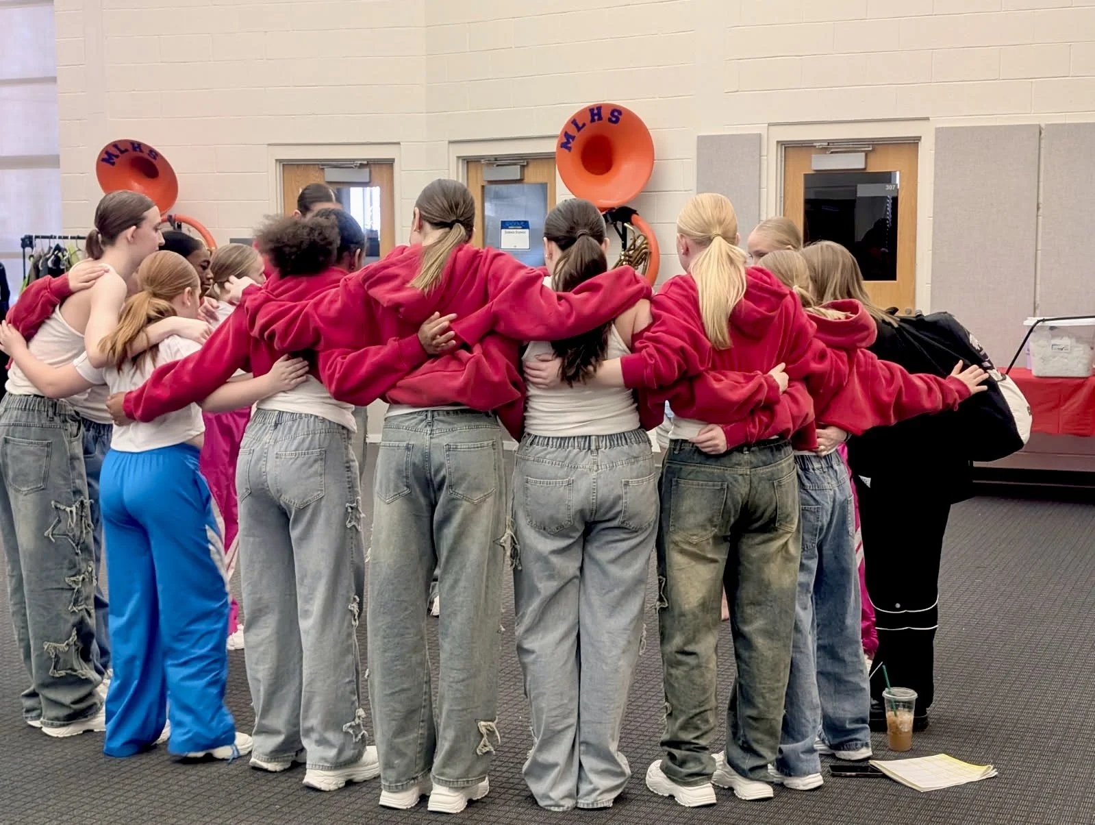 Group of girls in casual clothes standing in a circle with arms around each other in a huddle.