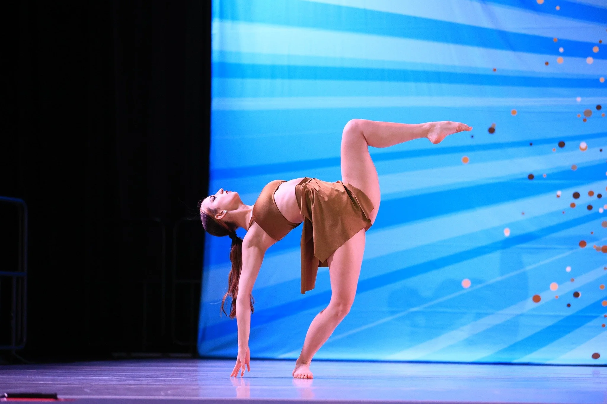 A female gymnast performing a one-handed balance pose on a stage with a blue background.