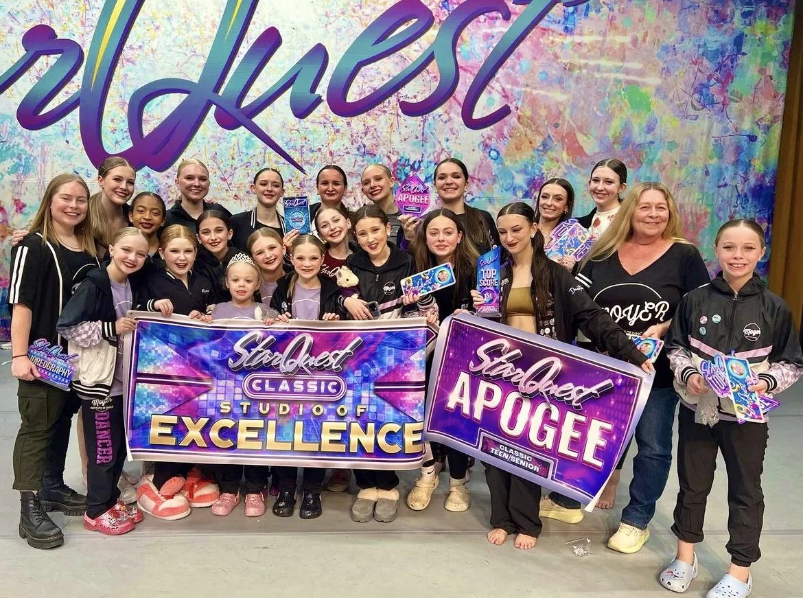 Group of young girls and an adult woman posing with awards and banners for Studio Quest dance competition, with a colorful backdrop that says "delves" in large cursive letters.