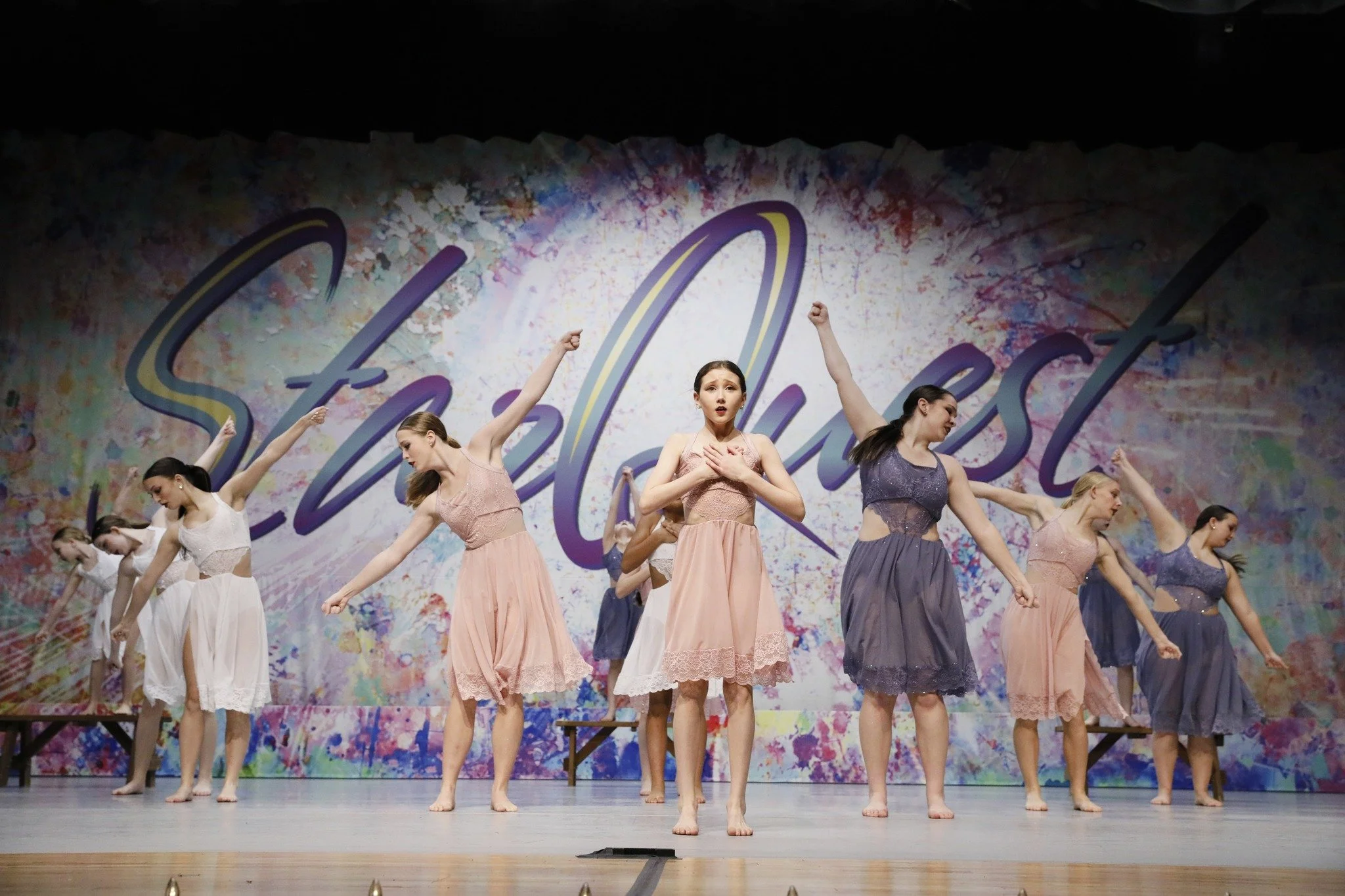 Group of young female dancers performing on stage with colorful backdrop that says 'Stella Lesa'.