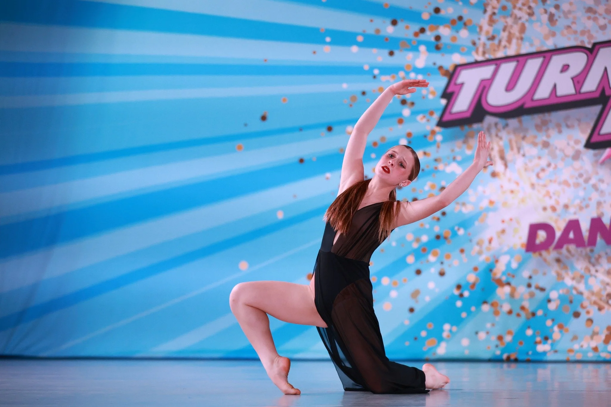 A female dancer performing a dance routine on stage with a colorful background and confetti decorations.