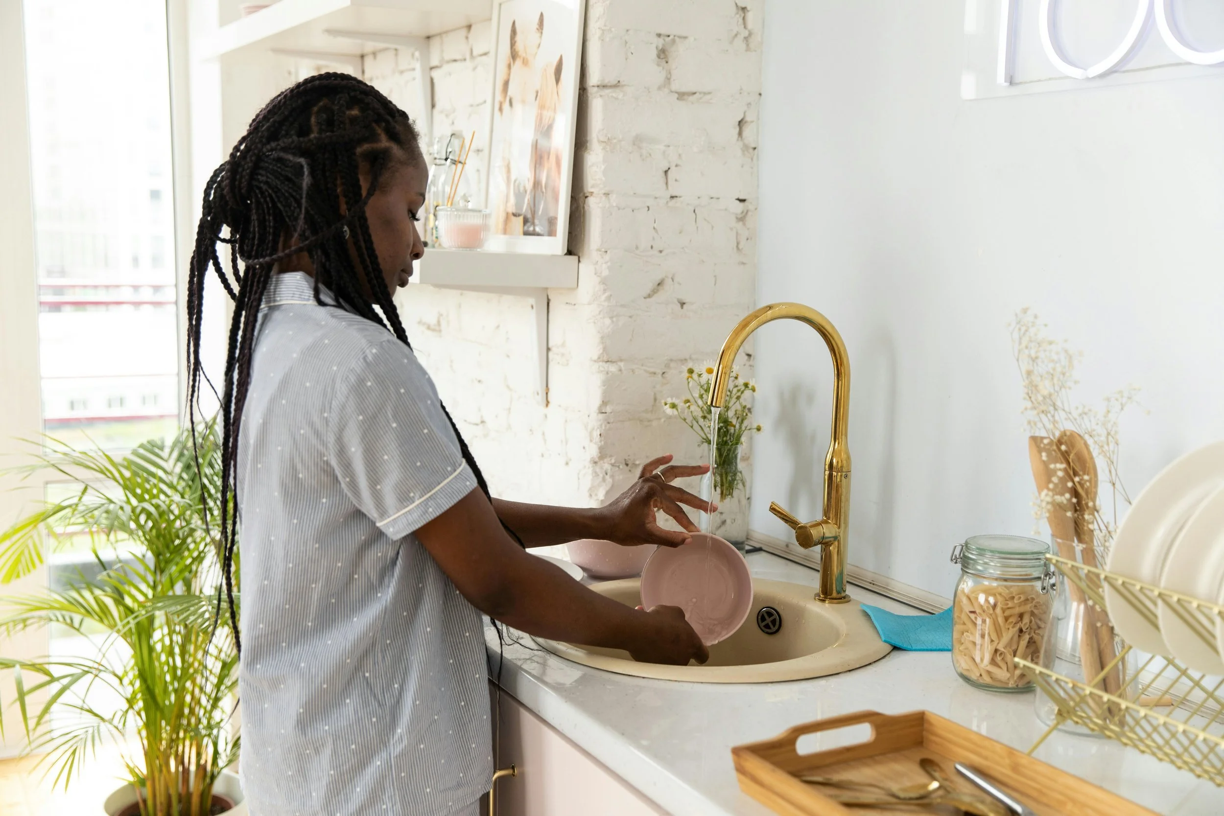 Black woman washing dishes alone, representing the quiet weight of carrying the household's emotional load