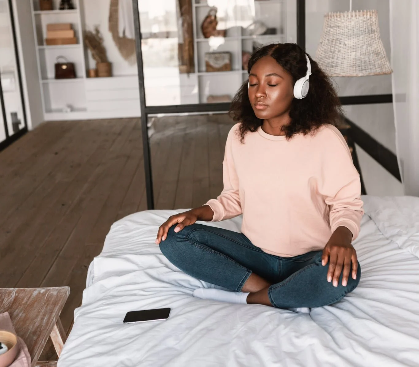 Woman sitting cross-legged in bed with eyes closed wearing headphones