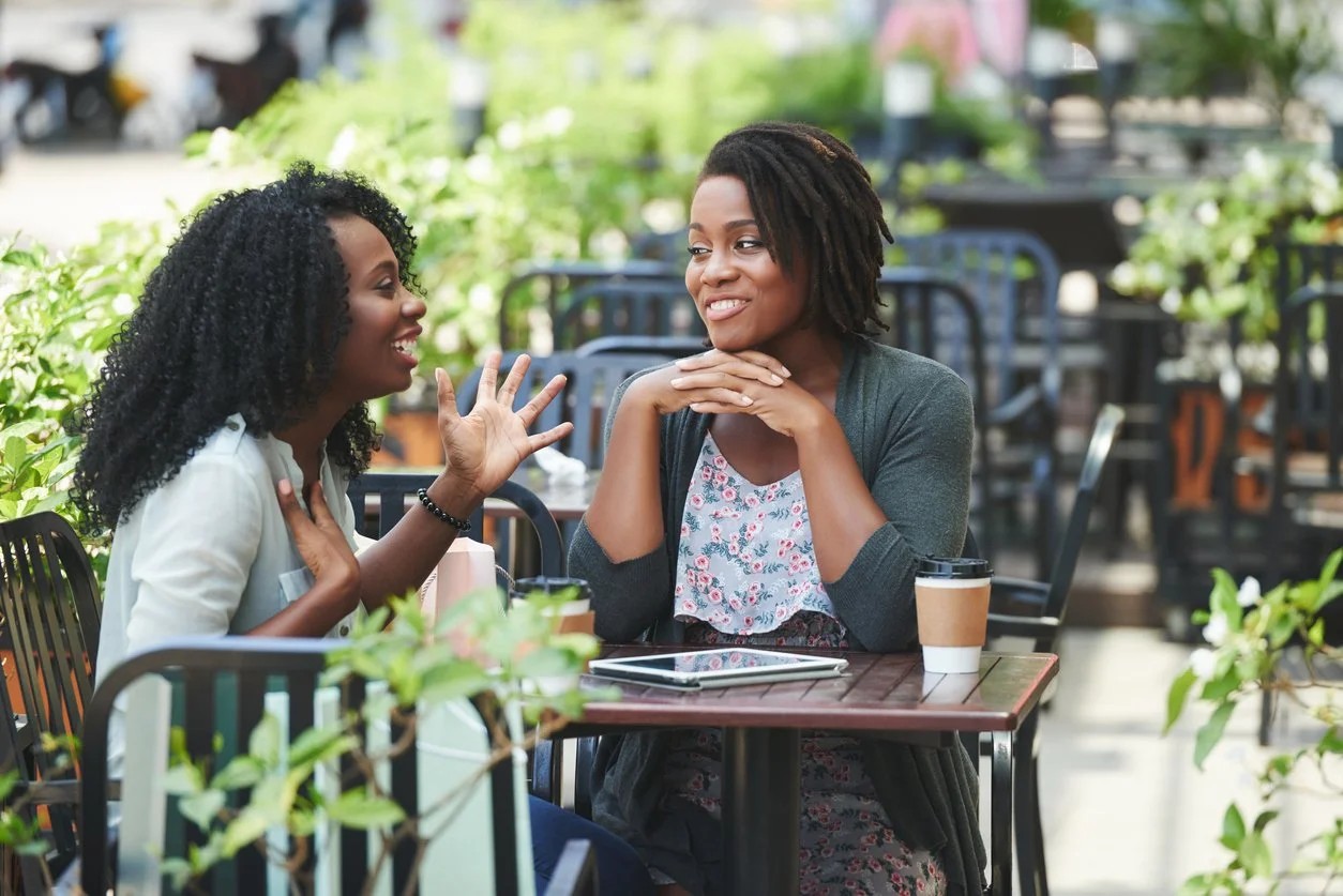 Two Black women eating outside at a restaurant, engaged in deep conversation, representing the reflective work of therapy