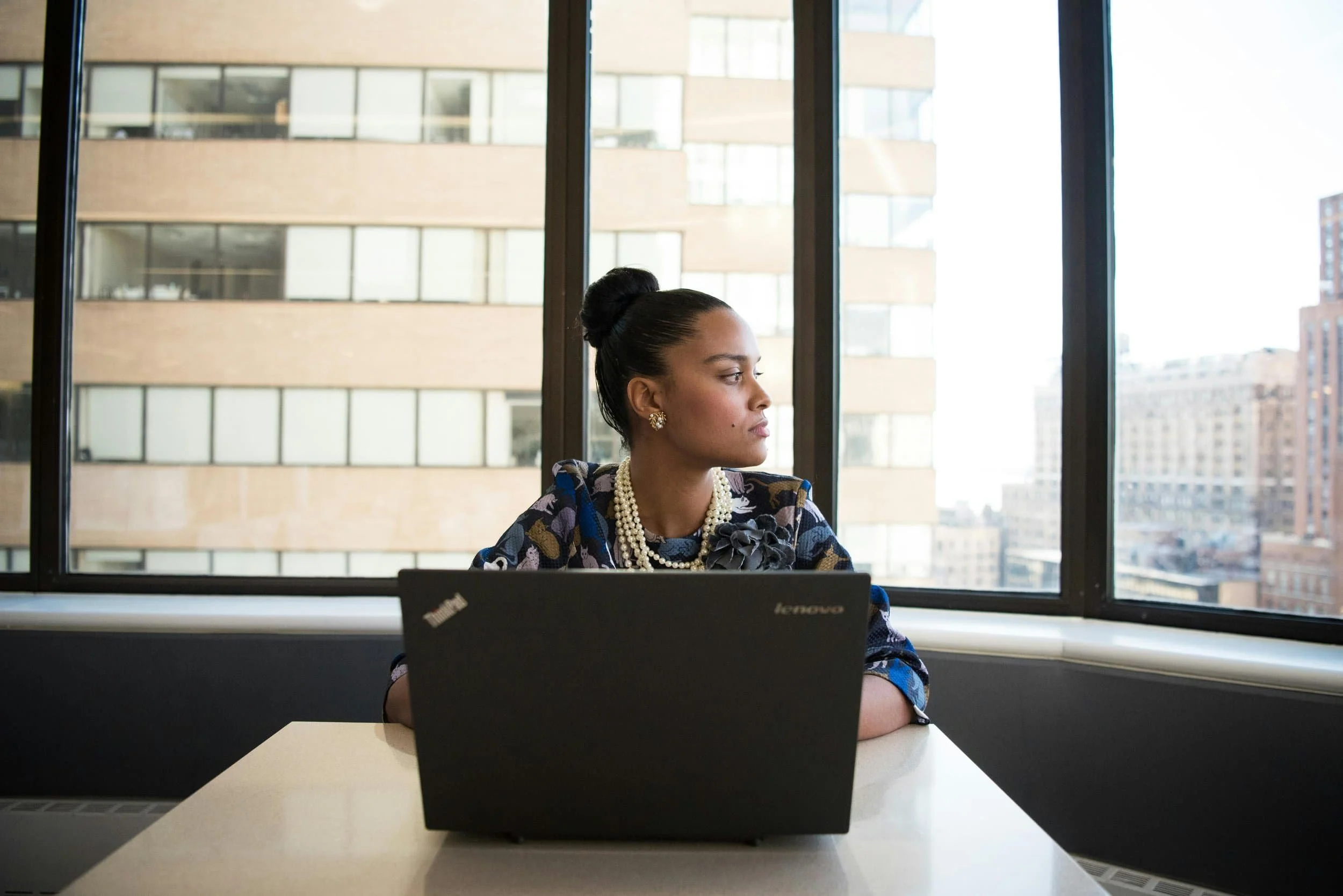 Woman sitting at a desk with a laptop open looking away in thought