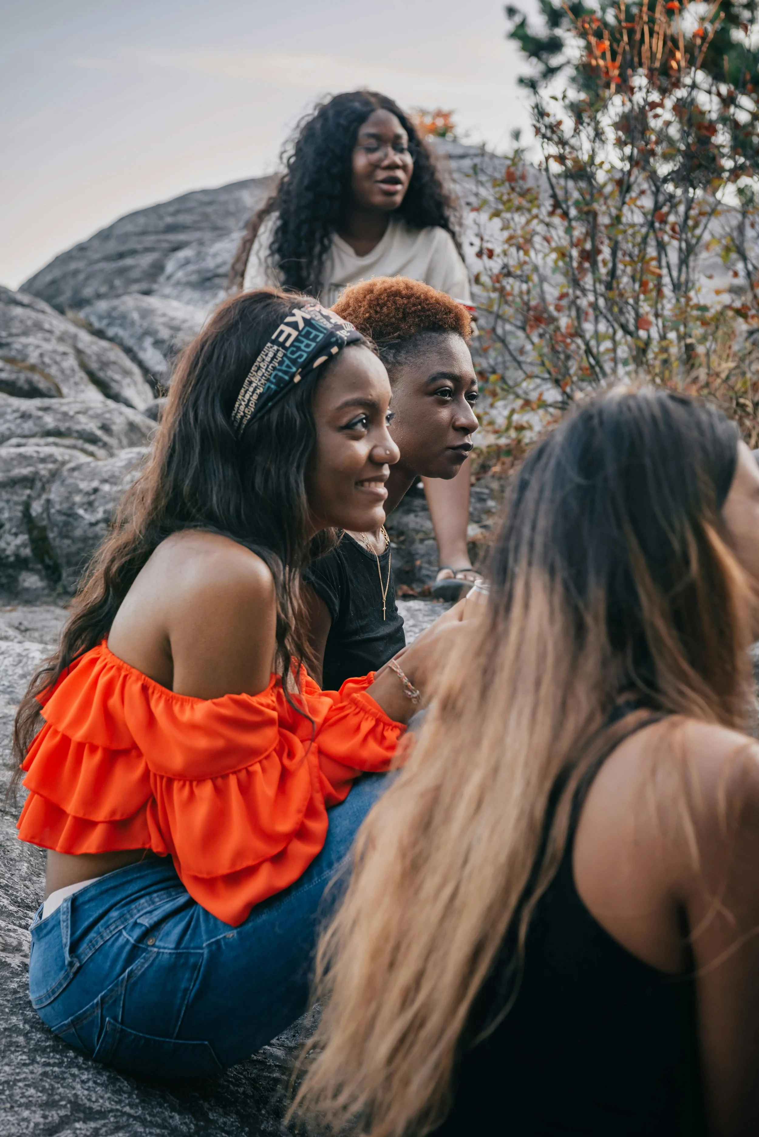 Black woman sitting outside with friends, looking thoughtful, reflecting the weight often carried in female friendships