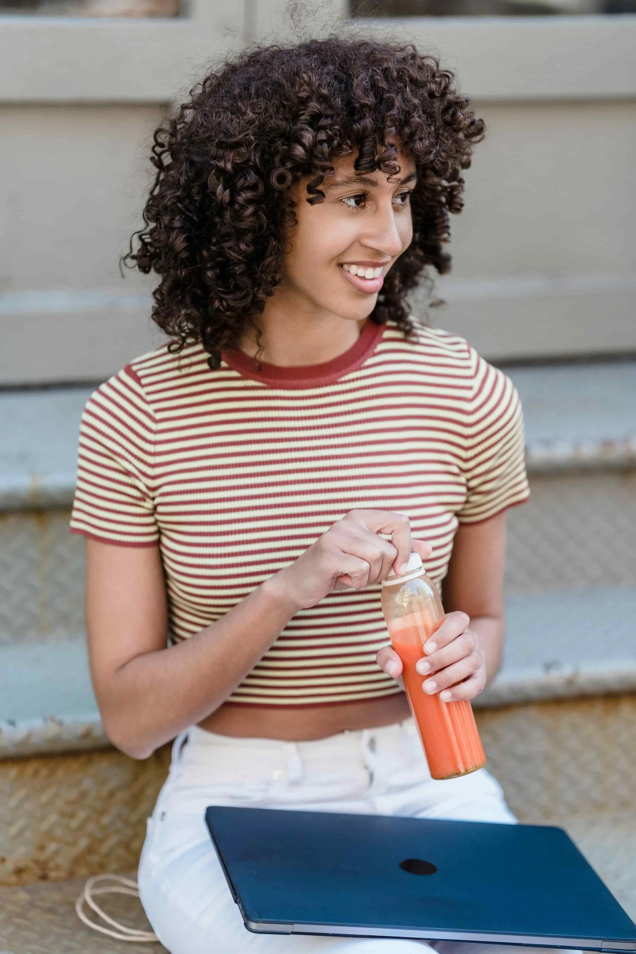 Woman sitting on outdoor stairs opening a bottle of juice
