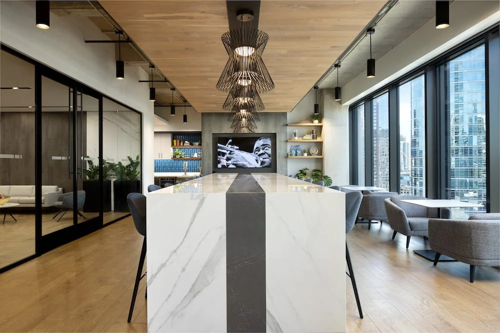 Modern hotel lobby or lounge area with large windows, seating, a marble central table, and contemporary lighting fixtures.