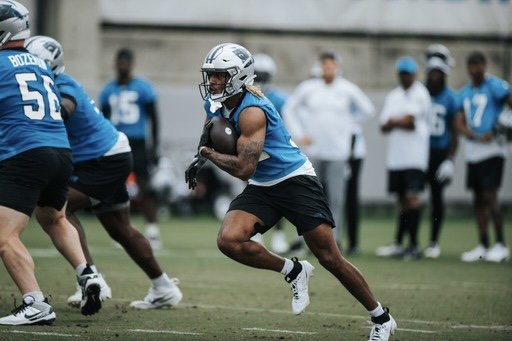 Football player in blue practice jersey running with football during a practice or game on the field.