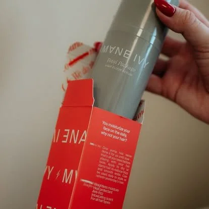 A hand holding a gray bottle of Jouviance Total Peptide Face Serum, with red packaging and some redness on the fingers.