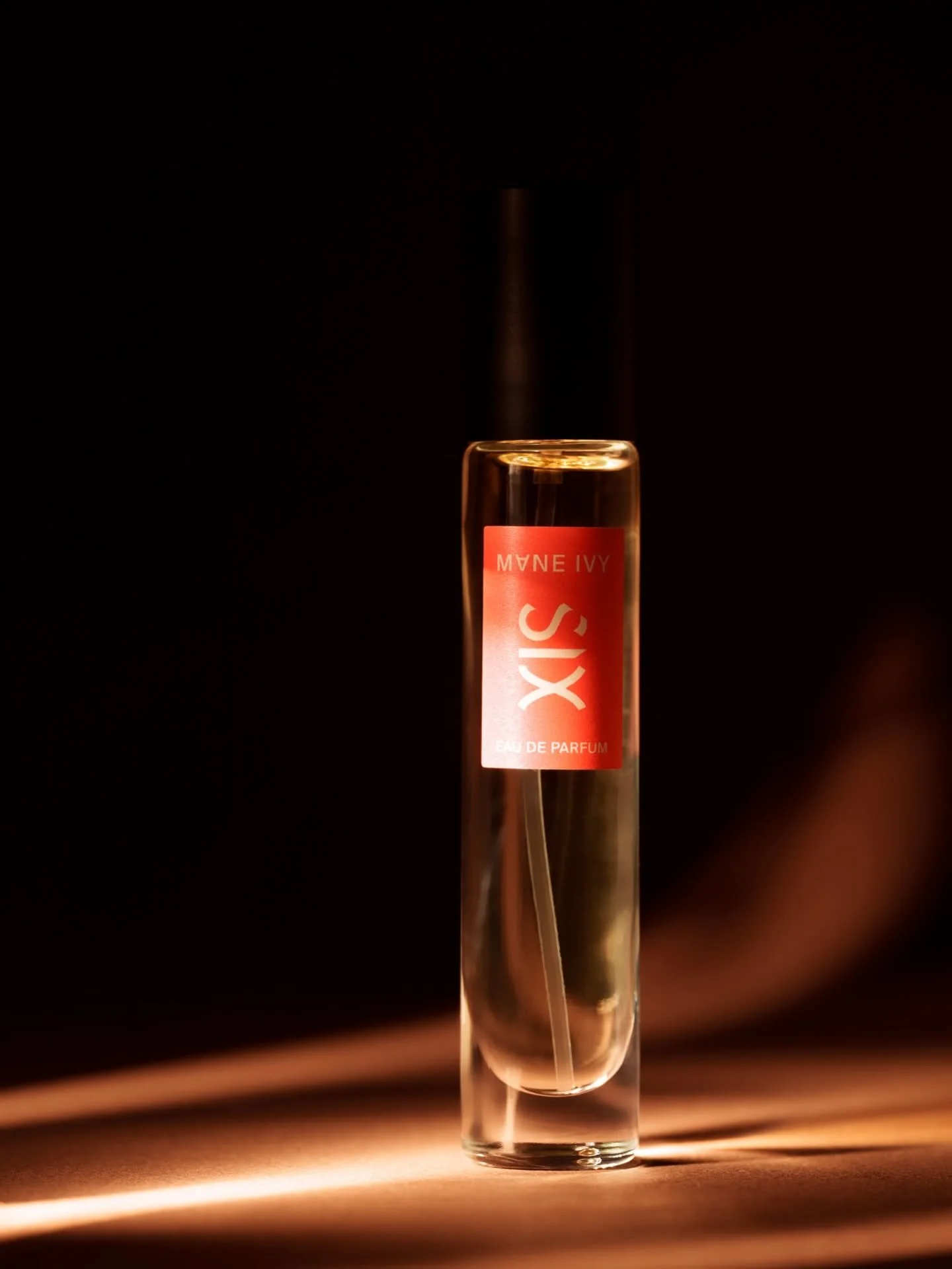 A tall, clear perfume bottle with a red label reading "IXS" and "Eau de Parfum" against a dark background, with light illuminating the bottle from the left.