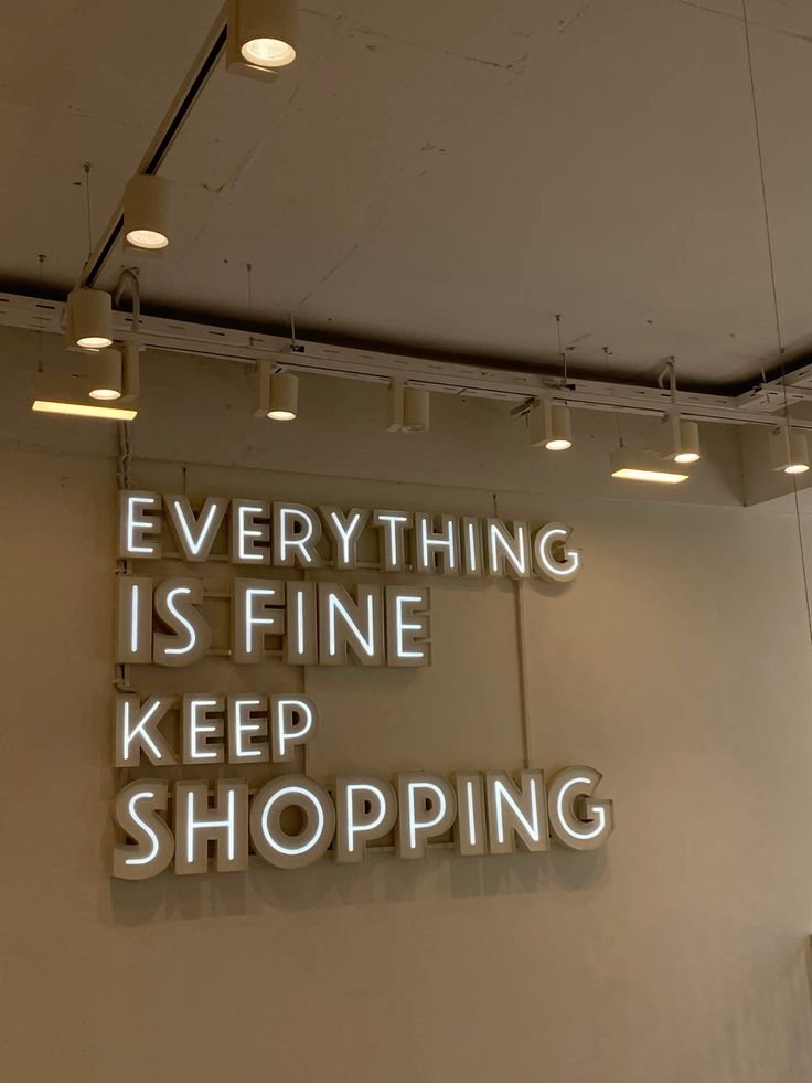 Illuminated sign on wall with the quote 'EVERYTHING IS FINE KEEP SHOPPING' in large white letters.