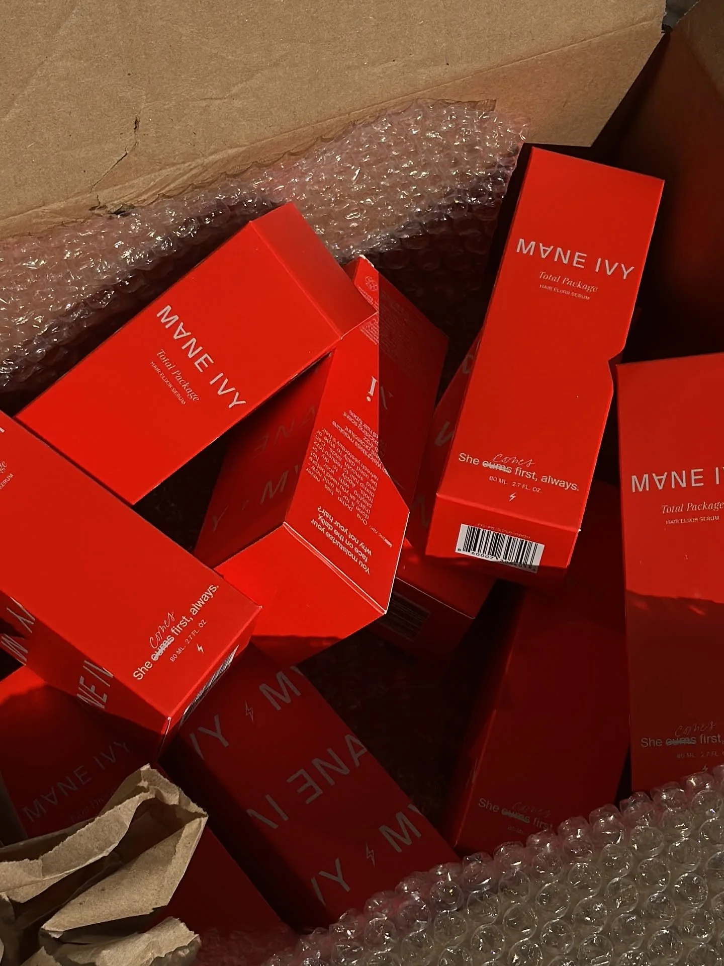Red boxes of she gloss serum inside a cardboard box surrounded by bubble wrap.