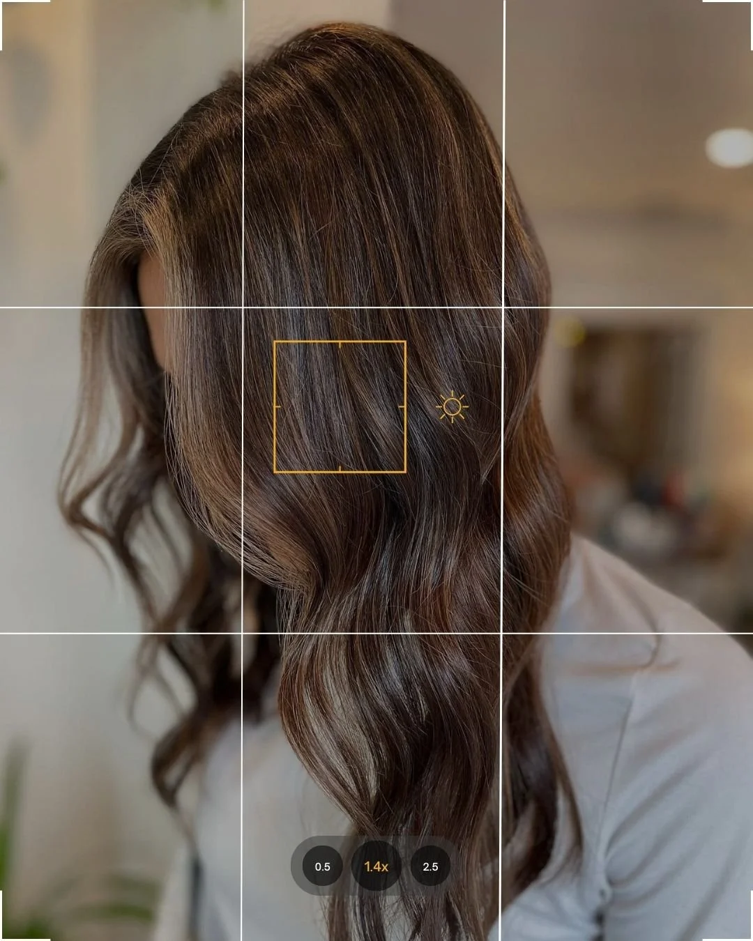 Close-up of a woman's wavy, brown hair with highlights, viewed through a camera or smartphone screen with focus settings visible.