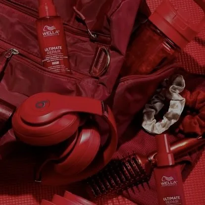 Red backpack containing hair care products, red headphones, and hair styling tools on a red surface.