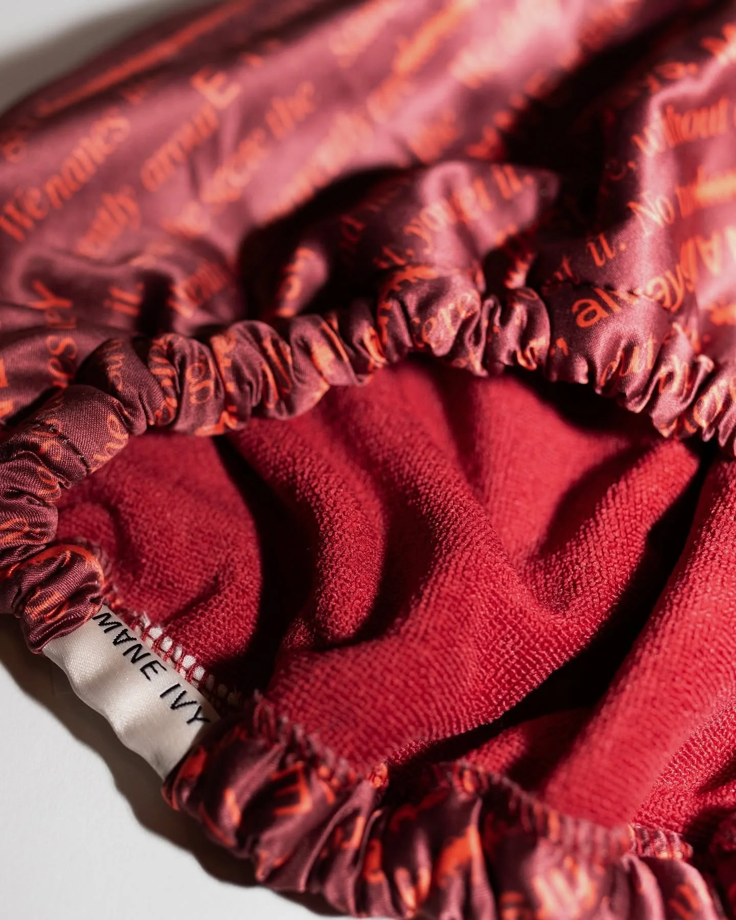 Close-up of a red fabric with printed orange text and a satin elastic scrunchie.