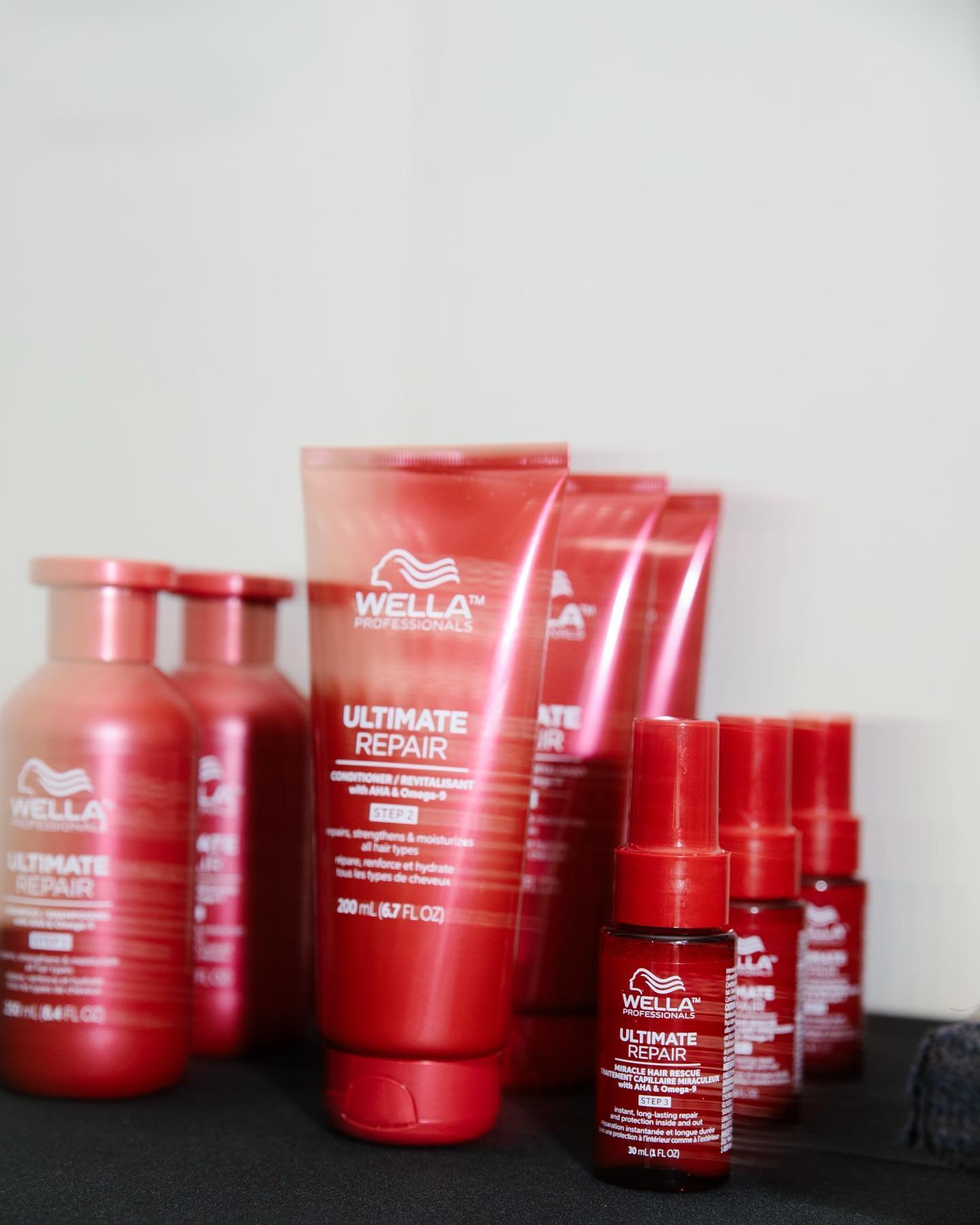 Multiple red bottles and tubes of Wella Professionals Ultimate Repair hair care products arranged on a black surface against a light background.