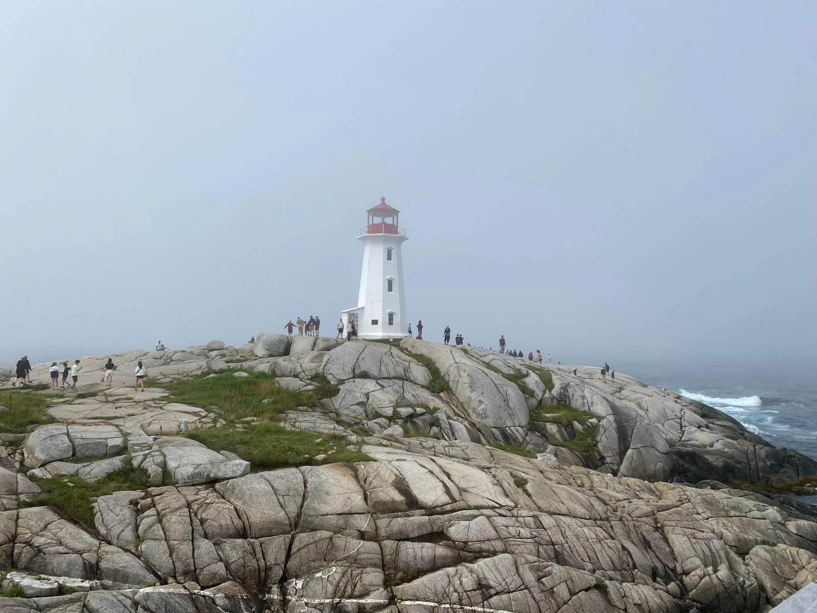 Faro bianco con tetto rosso su una scogliera rocciosa con nuvole e il mare sullo sfondo