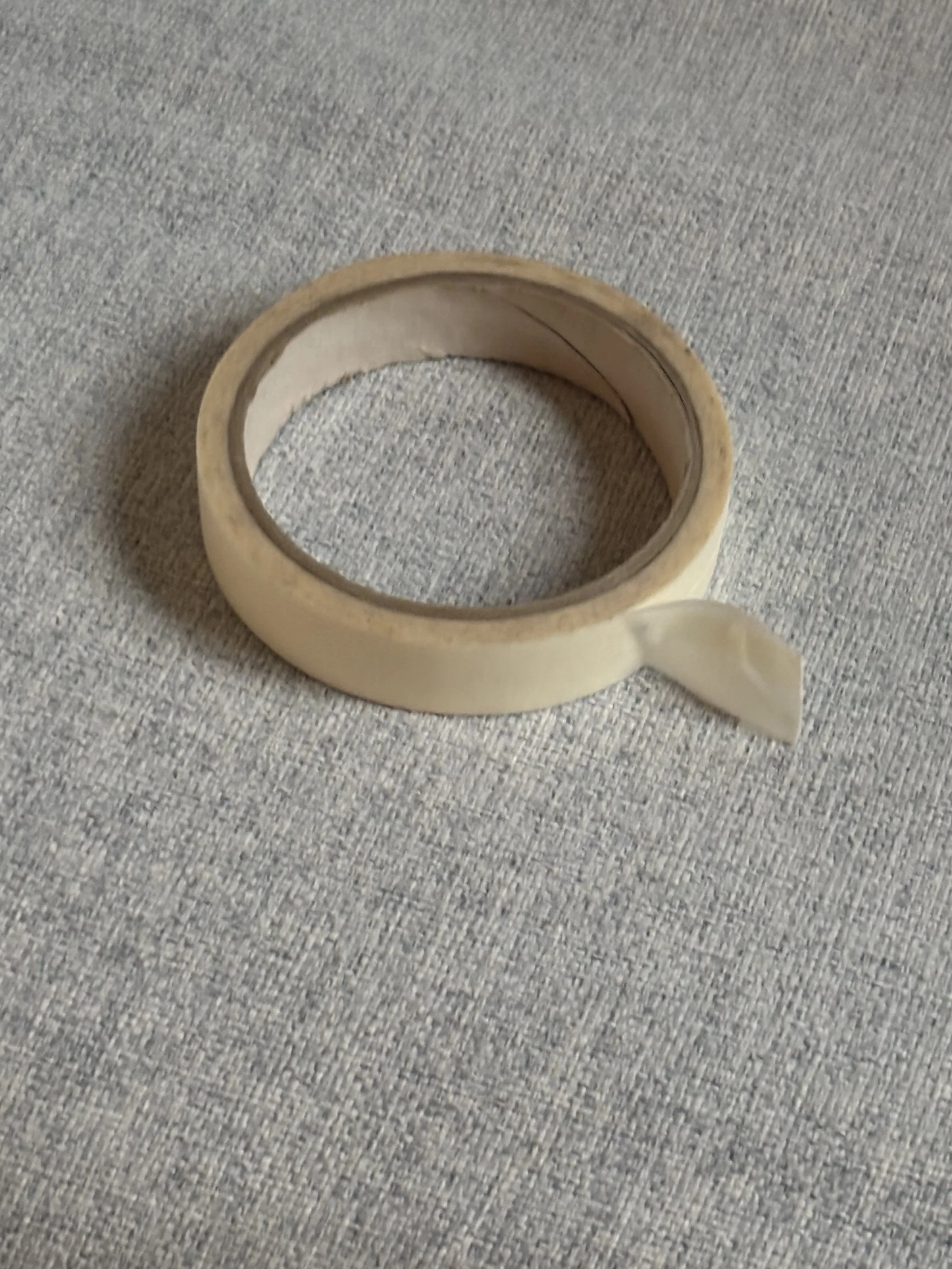 Cream-colored adhesive tape roll on a textured gray fabric surface.