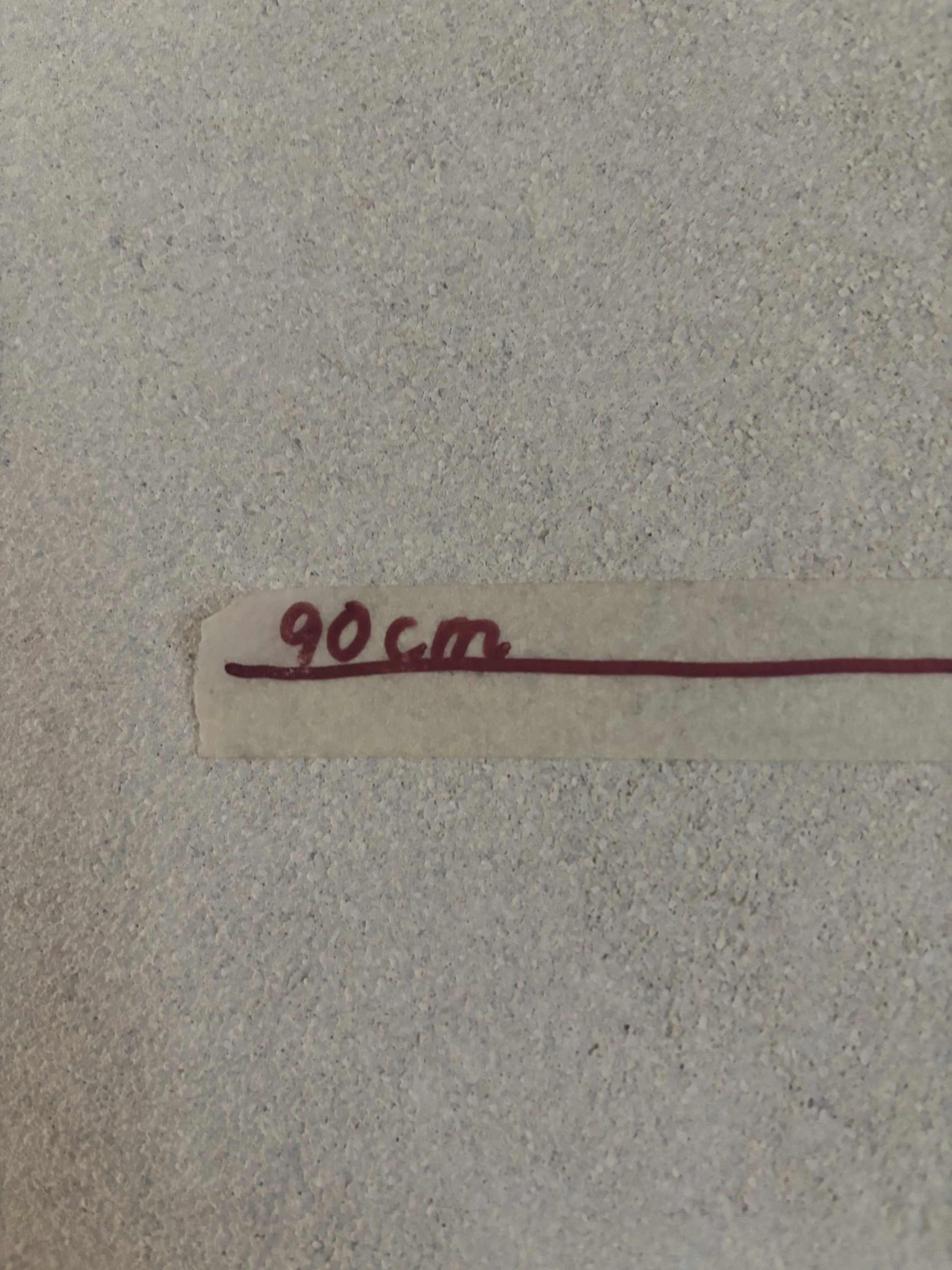 A small piece of masking tape with handwritten text reading '90cm' and a line drawn in red ink on a light-colored textured surface.