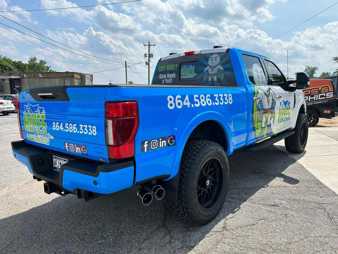 Blue commercial truck with cartoon mascot of a superhero gnome, advertising 'Hykes Gutters & Screens' with contact number 864-586-3338, social media icons, and the slogan 'Got Hail? Give Hank a Yell!'