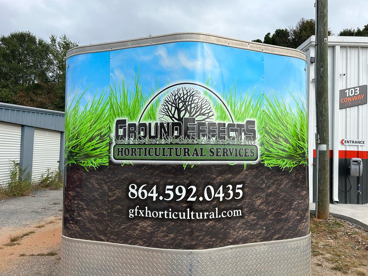 Sign on a trailer advertising Ground Effects Horticultural Services, with a tree and grass background, phone number 864.592.0435, and website gxfhorticultural.com.