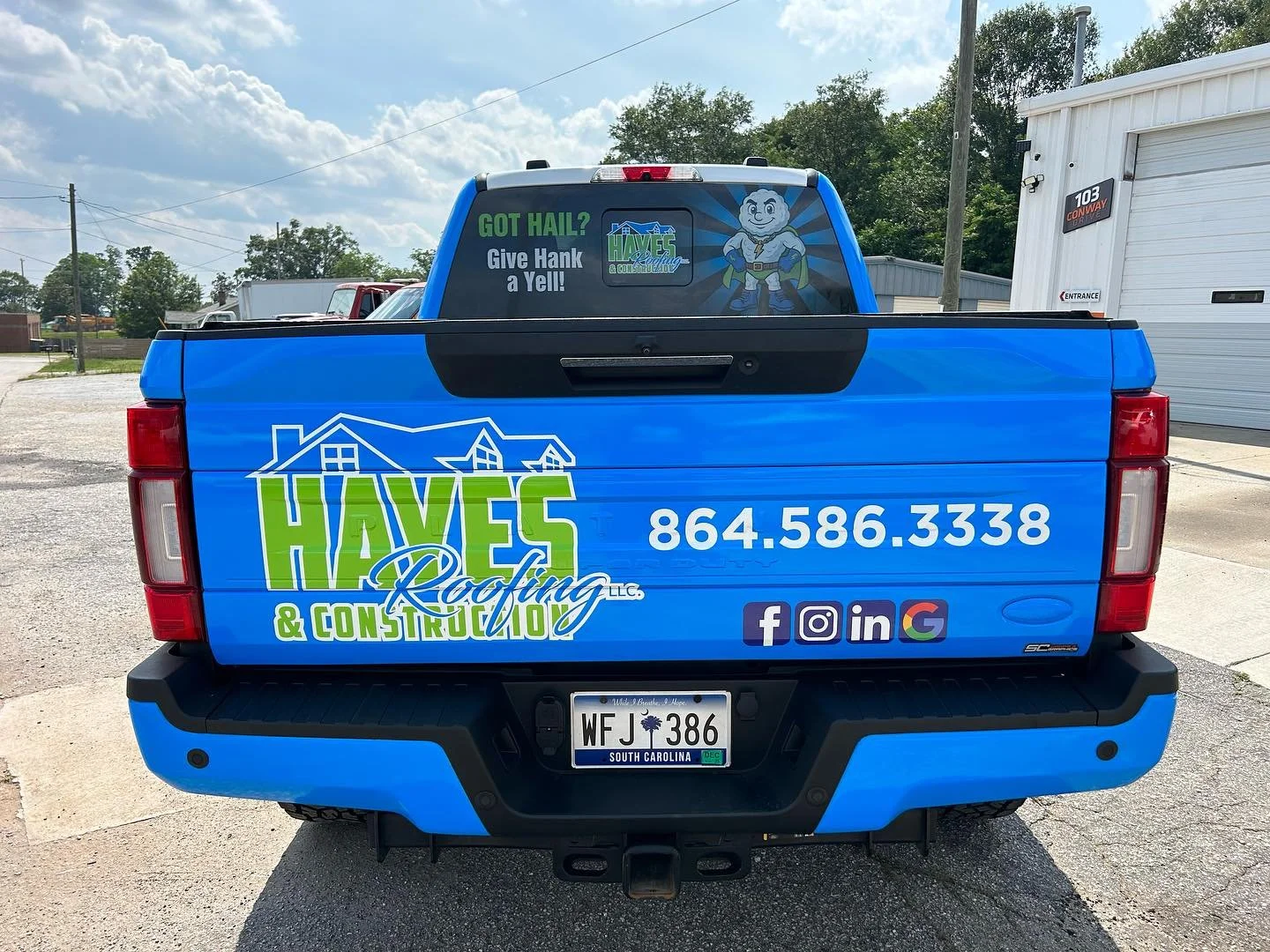 Blue pickup truck with Haves Roofing & Construction logo, phone number, and social media icons, parked outdoors with a building and trees in the background.