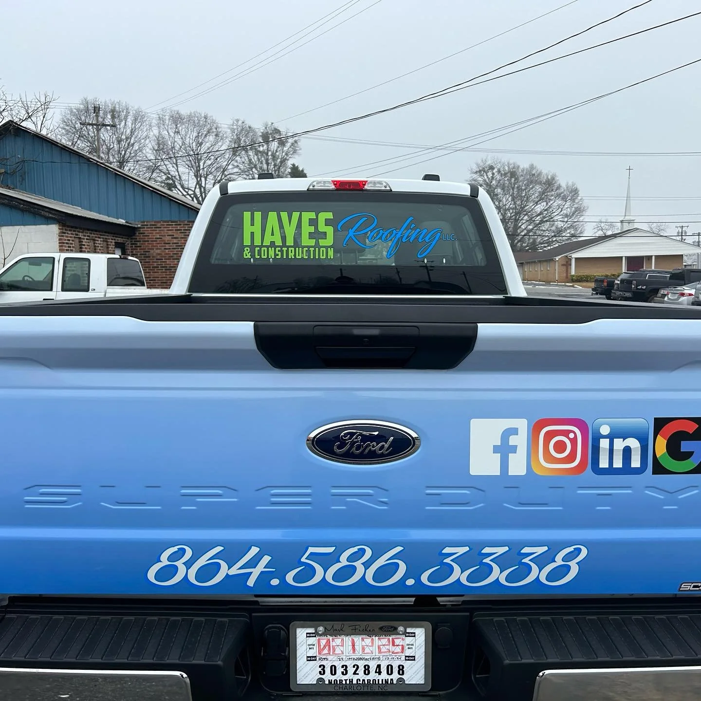 Back of a white Ford pickup truck with advertisements and social media icons on the tailgate. Window decal for Hayes Roofing & Construction in green and blue, and a phone number in white. Social media logos for Facebook, Instagram, LinkedIn, and Goog