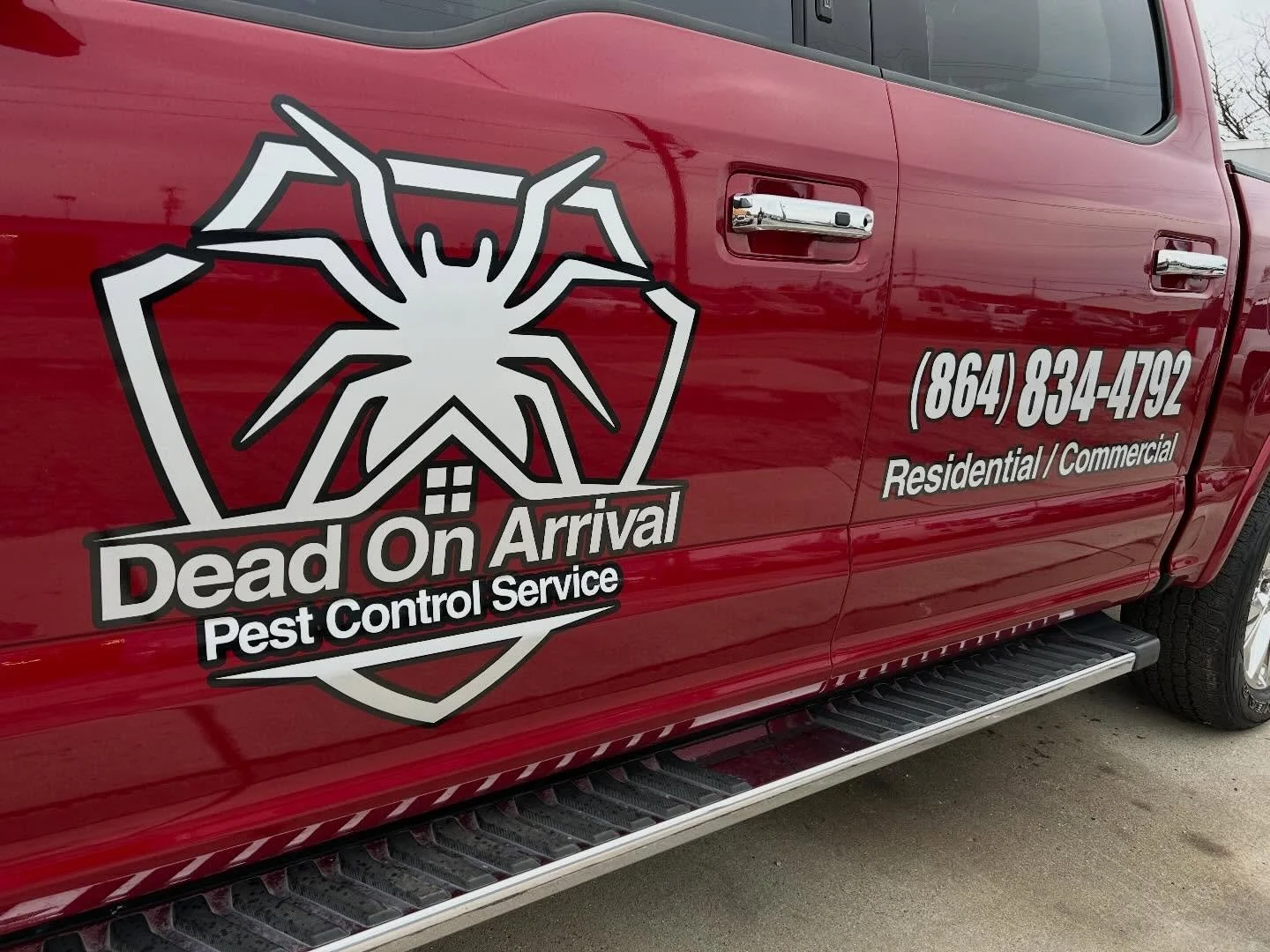 Red truck with a pest control company logo and contact information. The logo includes a large spider inside a shield, with the text 'Dead On Arrival Pest Control Service' and a phone number '(864) 834-4792' for residential and commercial pest control