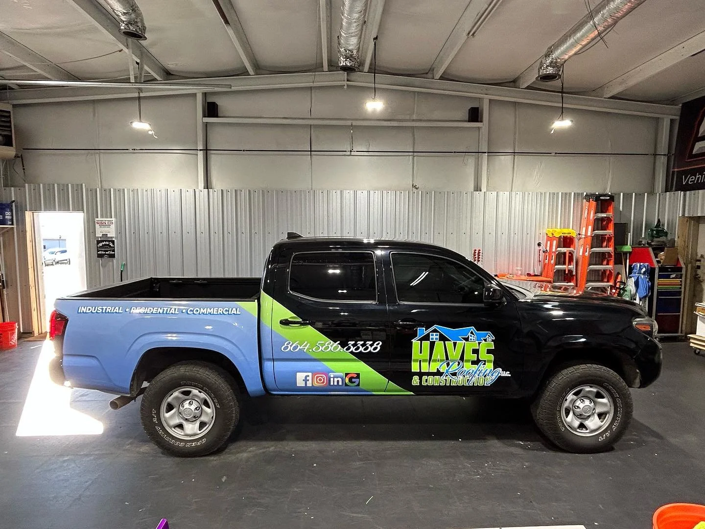A black pickup truck with colorful graphics and text that reads "Haves Roofing & Construction" parked inside a garage or workshop with tools and ladders in the background.