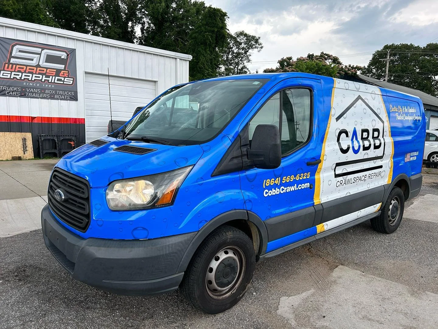 Blue 'Cobb Crawl' service van parked outside a building with a sign for SC Wraps & Graphics.
