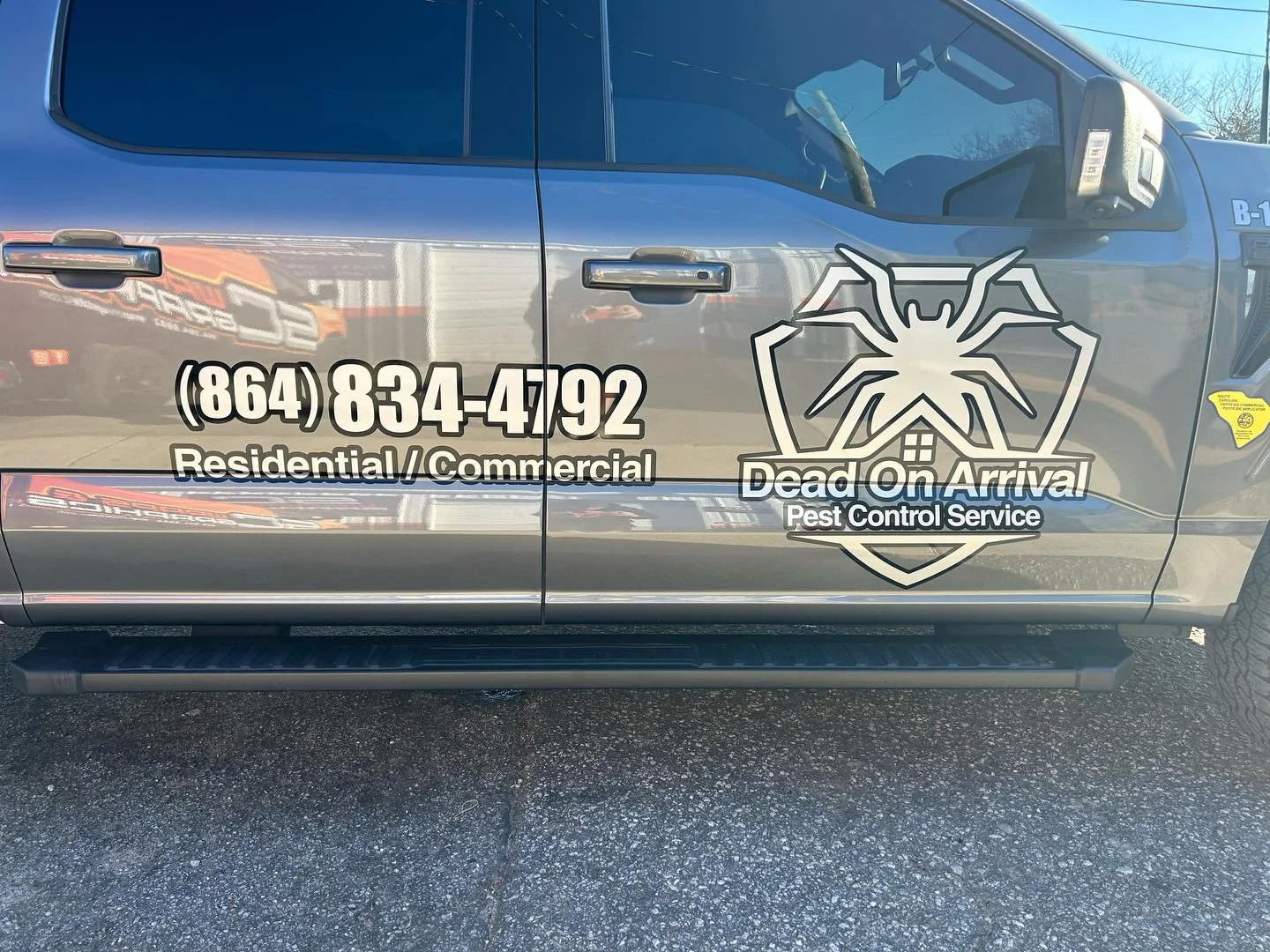 Gray pest control service vehicle with company logo, contact number, and description of services including residential and commercial pest control, parked on asphalt.