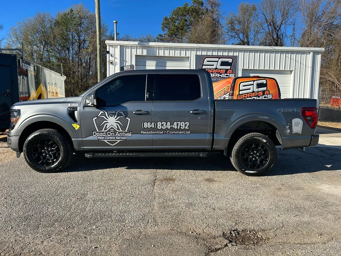 Gray pickup truck with pest control company logo and contact information parked outside a building with 