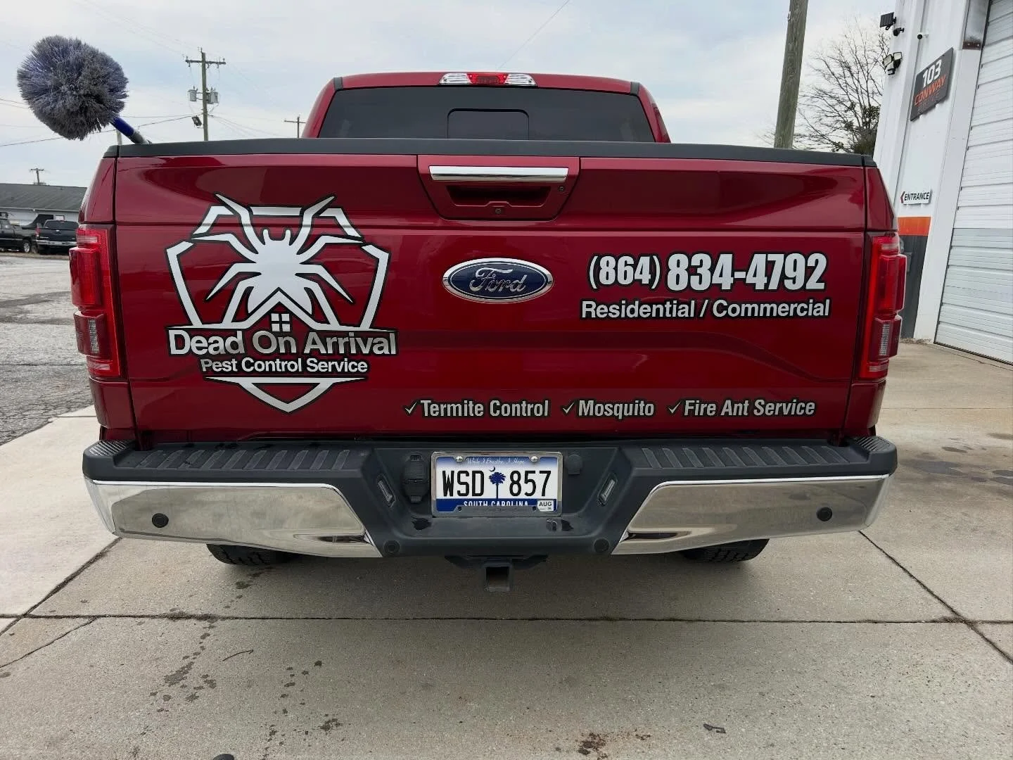 Red pickup truck with advertising for Dead On Arrival Pest Control Service, featuring a large spider logo, phone number, and services such as termite control, mosquito control, and fire ant service. South Carolina license plate.