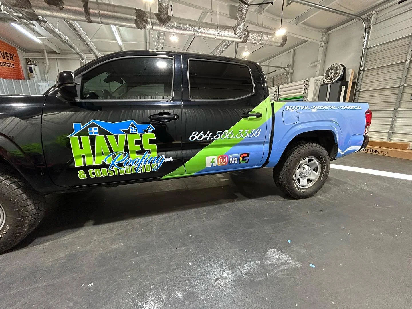 Truck with colorful wrap advertising Haven Roofing & Construction, featuring a black cab, cityscape graphics, contact information, social media icons, and a blue and green theme in an indoor garage.