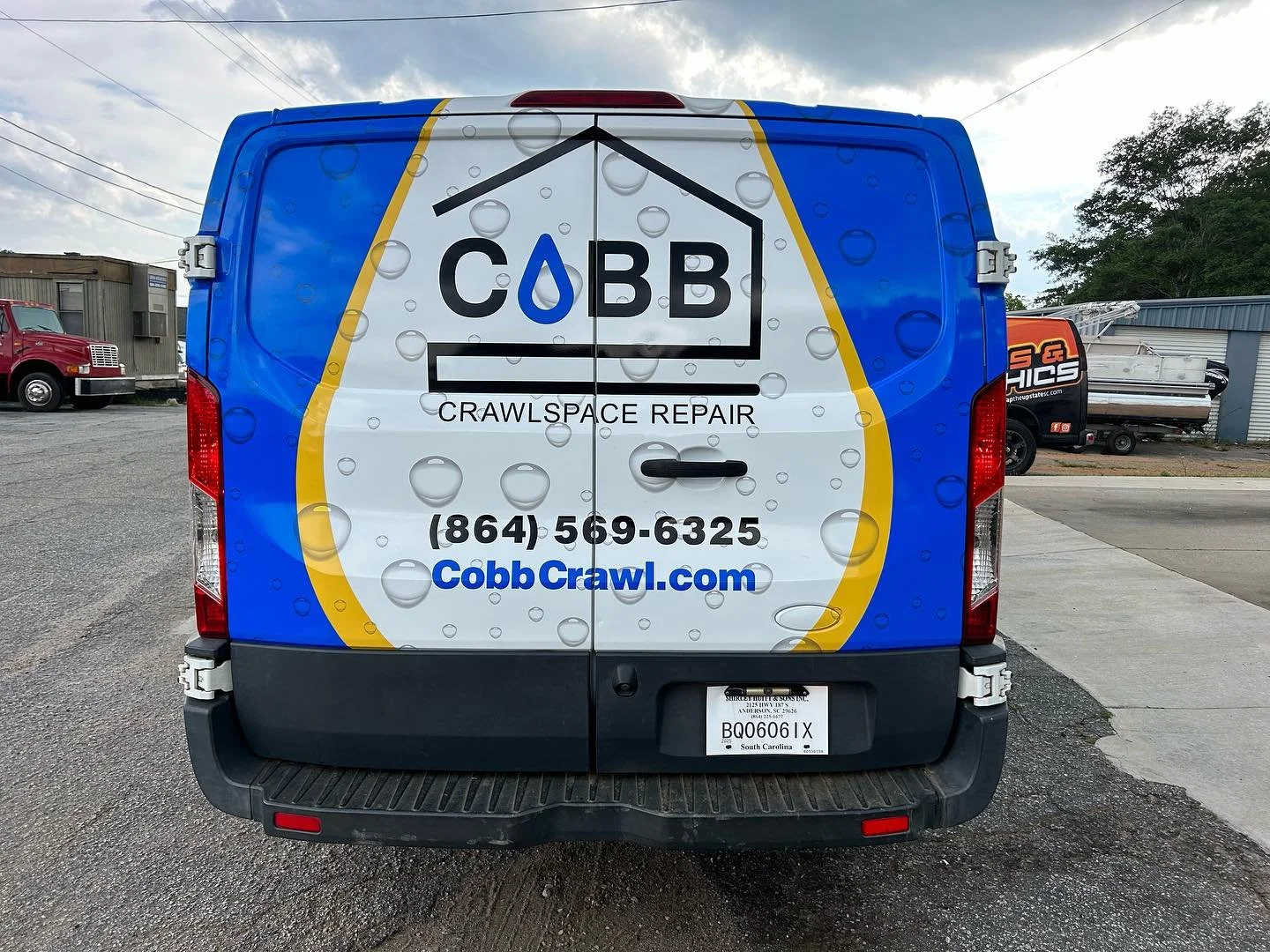 The back of a white and blue service van for Cobb Crawl, a crawlspace repair company. The van features a black house outline with a water droplet inside the letter 'O' in Cobb. The company's contact number, website, and a leaf emblem are displayed on