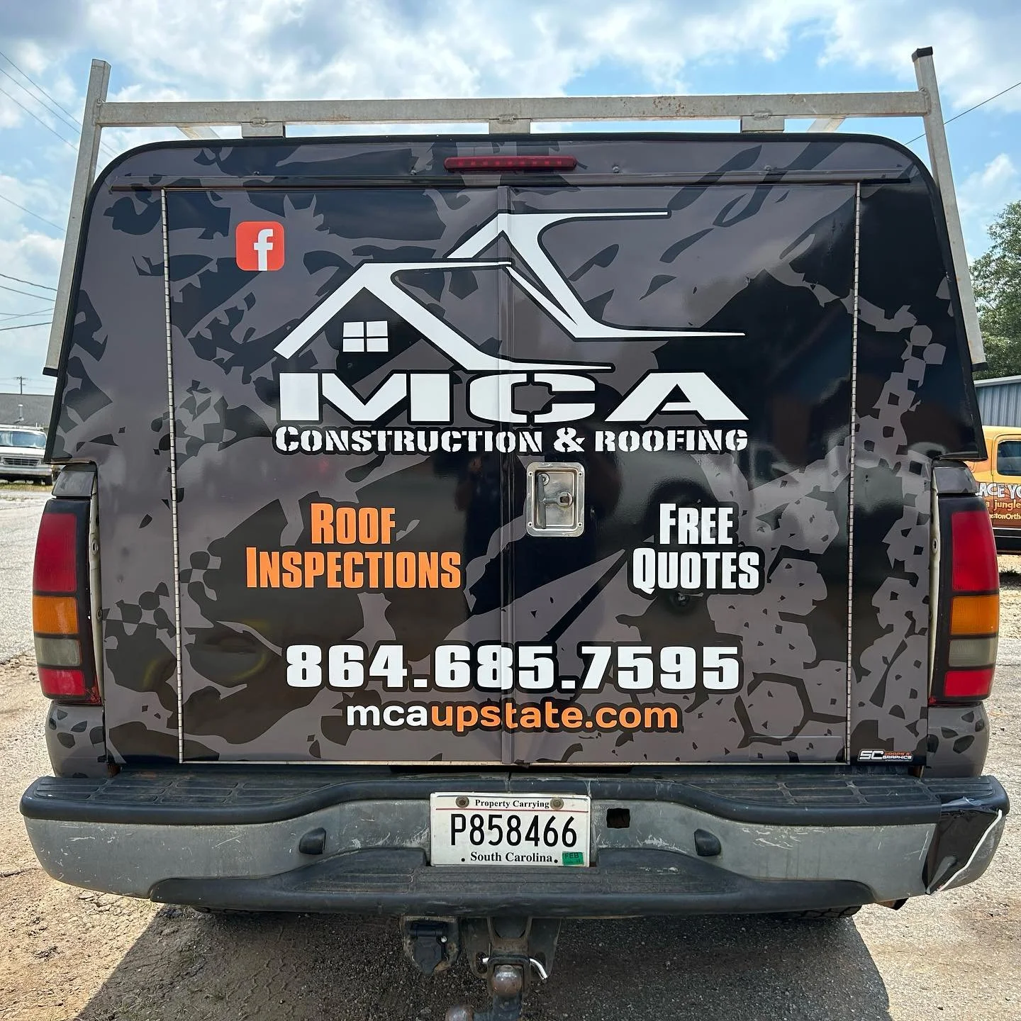 A black truck with a large advertisement for MCA Construction & Roofing on its back. The advertisement includes the company logo, phone number, website, and promotional text for roof inspections and free quotes.